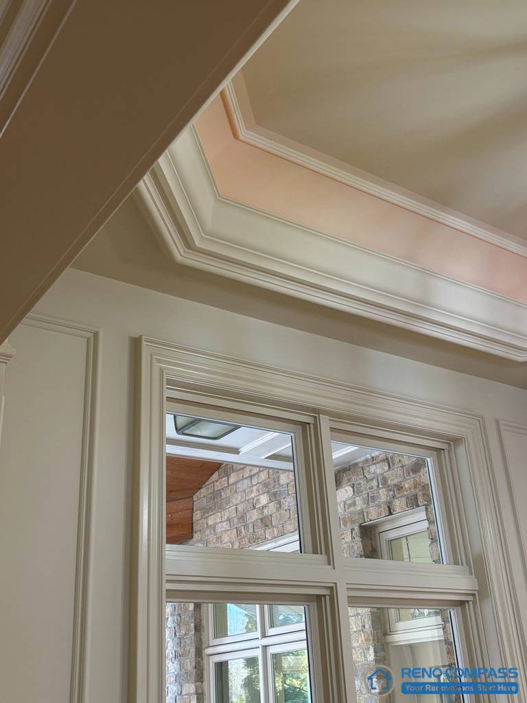 This image captures the junction between a European-style ceiling detail and classically framed windows, highlighting layered moulding, wall panelling, and precise trim alignment. The recessed ceiling treatment is carefully proportioned to the window height, reinforcing architectural hierarchy and visual order. Natural light interacts with the moulded surfaces, revealing depth and craftsmanship without relying on decorative excess. This detail view demonstrates refined construction and disciplined detailing within a high-end Richmond Hill interior renovation grounded in traditional European architectural principles.
