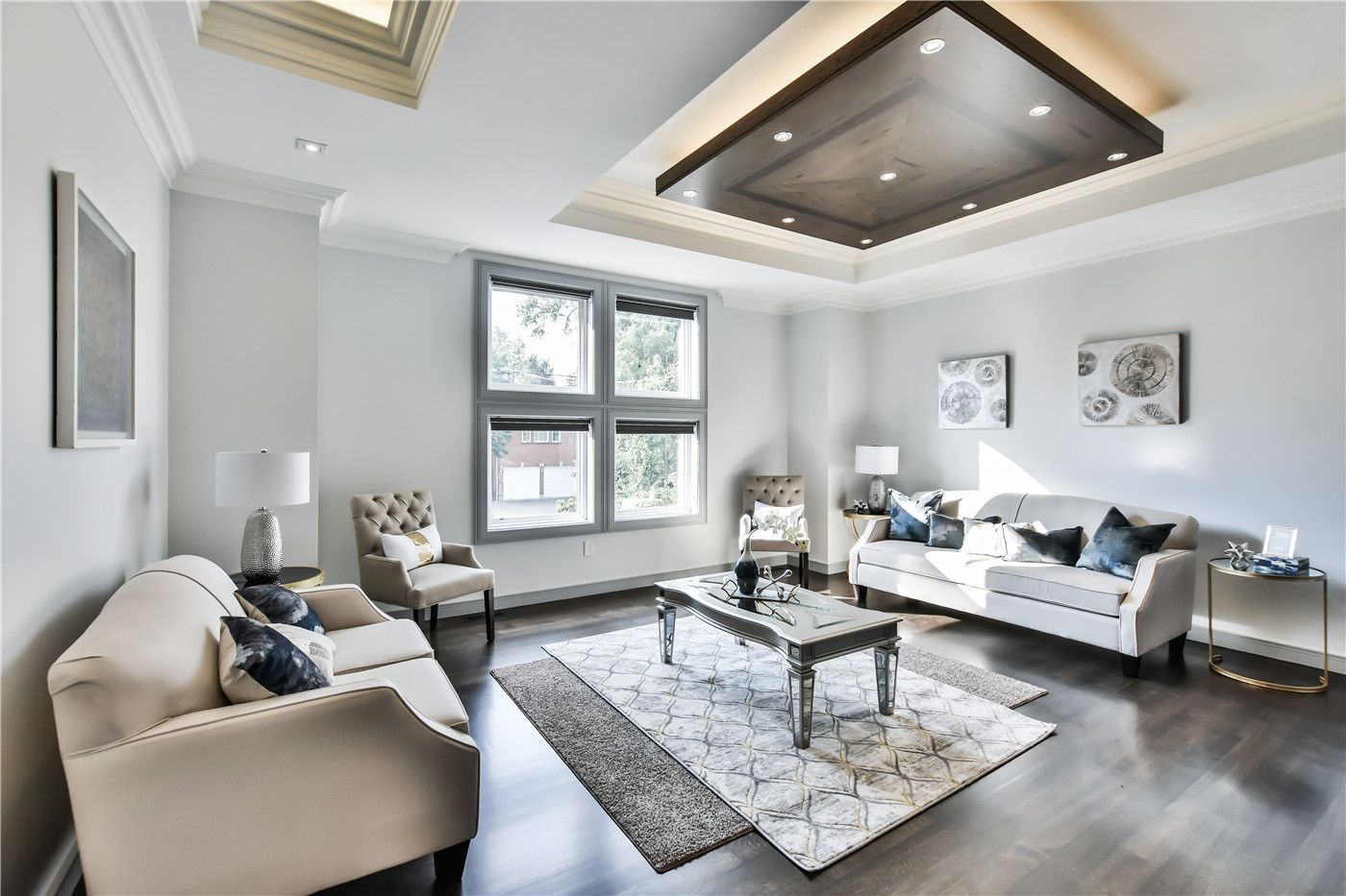 This Toronto interior design pre-sale staging features a luxury living room with a stunning coffered ceiling, recessed lighting, and modern neutral-tone furniture. Large windows provide abundant natural light while elegant décor, hardwood flooring, and a balanced layout create a bright and sophisticated atmosphere.