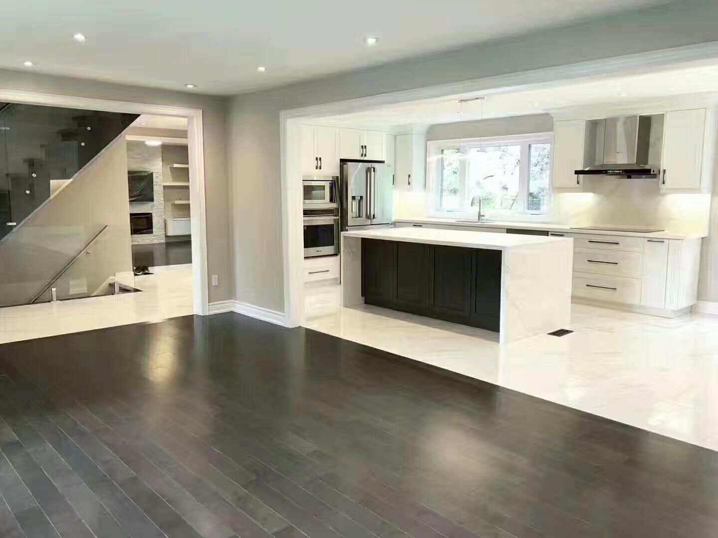 This Markham interior renovation features a bright open-concept layout that seamlessly connects the kitchen, dining, and living areas. The modern kitchen includes a large quartz island, custom white cabinetry, built-in stainless steel appliances, and recessed ceiling lighting. Dark hardwood flooring contrasts with light stone tiles, enhancing depth and visual flow throughout the space. Designed to improve functionality, natural light, and everyday comfort, this renovation reflects the craftsmanship of a professional Toronto renovation company delivering high-quality interior transformations.