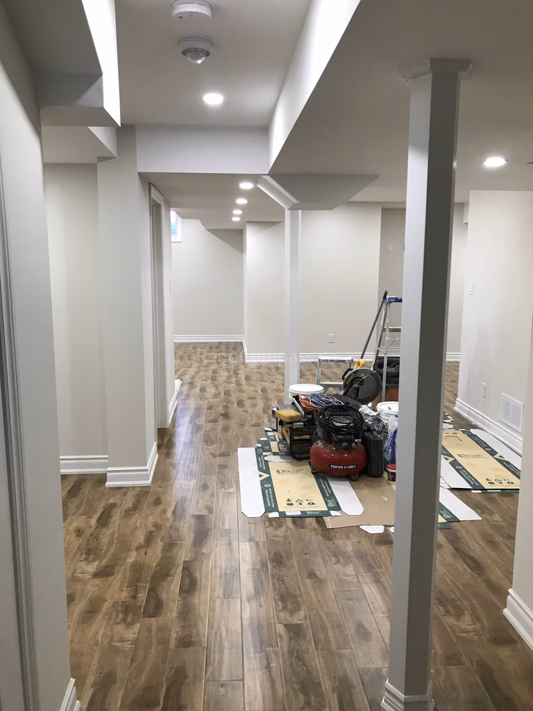 This Toronto basement renovation showcases a newly finished hallway with modern flooring, recessed pot lights, and clean wall and ceiling detailing. The upgraded layout improves flow and functionality while creating a bright and welcoming lower-level living space. Completed by Reno Compass, a professional Toronto renovation company, this project highlights quality craftsmanship and practical basement design for modern homes.