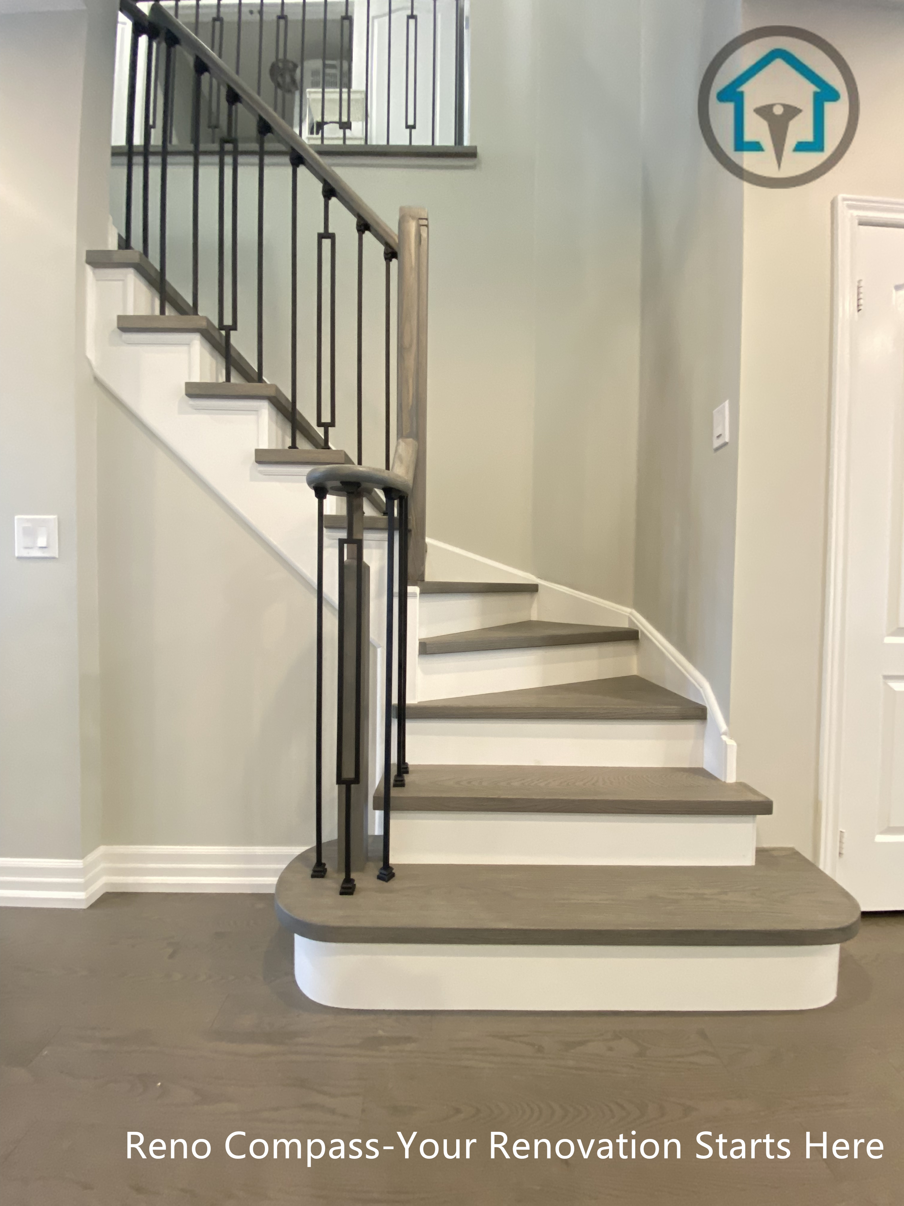 This custom staircase renovation features a gently curved entry step, warm wood treads, and slim black metal balusters that bring structure and elegance to the space. The curved base softens the transition between floors while improving circulation and visual balance. Clean white risers and consistent detailing create a refined, cohesive look that integrates seamlessly with the surrounding interior finishes, completed as part of a full-home renovation by Reno Compass.