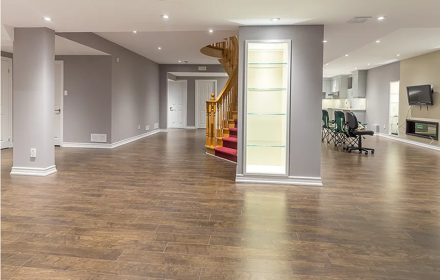 Elegant open-concept basement renovation in Toronto featuring upgraded hardwood flooring, custom staircase with wood railing, recessed pot lights, and built-in glass display niches. The spacious layout connects entertainment, living, and kitchen areas for modern functionality and comfort. This professionally finished basement highlights quality craftsmanship by a trusted Toronto renovation company specializing in complete basement renovations and interior remodeling.