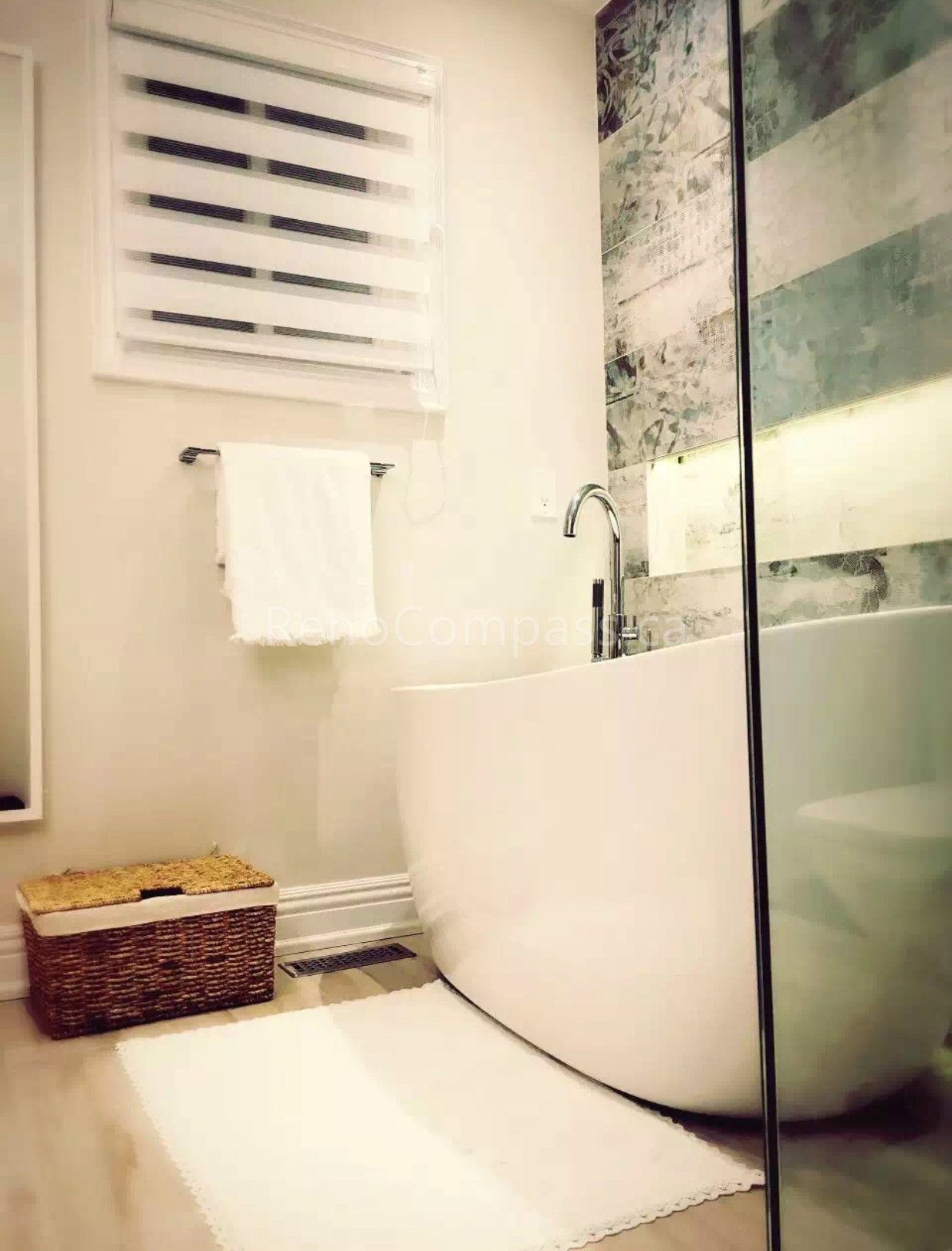 A minimalist bathroom interior renovation in Toronto featuring a freestanding bathtub, glass shower enclosure, soft neutral tones, and natural wood flooring. The design highlights clean aesthetics, functional layout, and spa-like comfort, reflecting modern Toronto interior renovation and interior design standards.