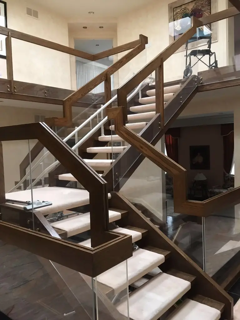 This Toronto interior renovation features a beautifully crafted custom staircase with rich wood framing, glass panel railings, and elegant light-toned stair treads. The multi-level open design enhances visual flow while maintaining safety and durability. Modern glass guardrails allow natural light to travel throughout the space, creating a bright and sophisticated interior atmosphere. Completed by a professional Toronto renovation company, this staircase renovation highlights detailed craftsmanship, structural precision, and contemporary residential design.