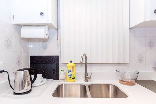 This Toronto interior renovation features a clean and functional kitchen sink area with white cabinetry, tiled backsplash, and a modern stainless-steel double sink. The bright layout improves everyday usability while maintaining a neat and minimalist aesthetic. The renovation enhances both practicality and comfort, creating an efficient kitchen space for modern Toronto home living.