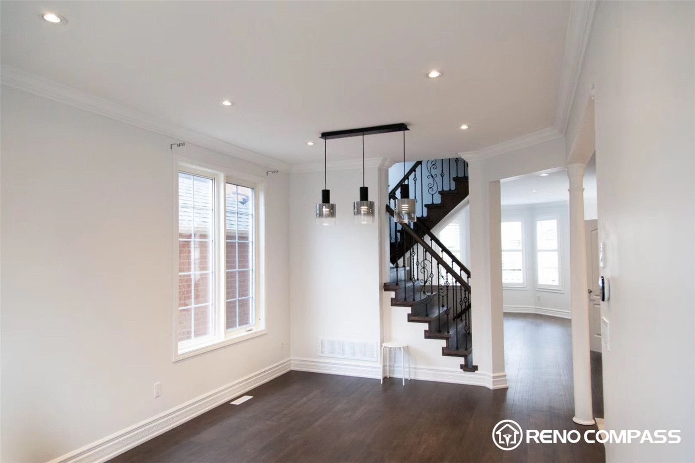This Markham interior renovation features an open concept layout connecting the living and dining areas with seamless hardwood flooring. The space is enhanced by modern pendant lighting, large windows for natural light, and a stylish staircase with iron railings, creating a clean, spacious, and contemporary home environment.