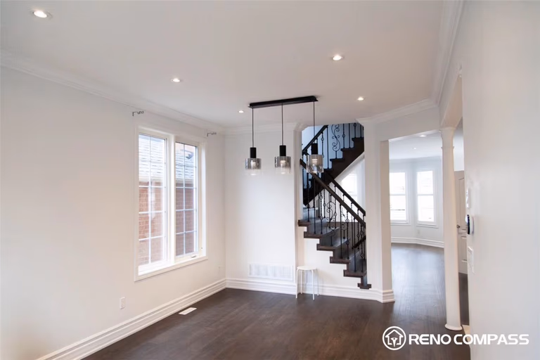 This Markham interior renovation features an open concept layout connecting the living and dining areas with seamless hardwood flooring. The space is enhanced by modern pendant lighting, large windows for natural light, and a stylish staircase with iron railings, creating a clean, spacious, and contemporary home environment.