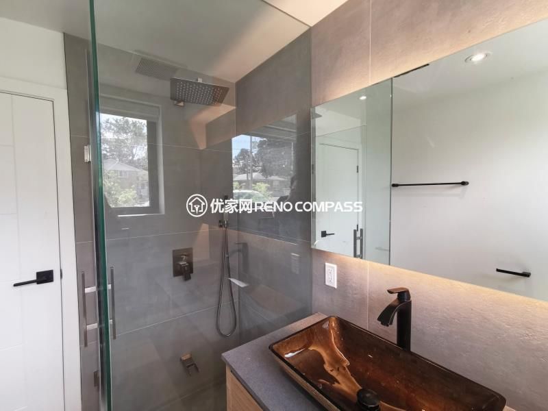 Modern bathroom completed as part of a North York interior renovation, featuring a frameless glass shower enclosure, large-format wall tiles, and a custom vanity with vessel sink. The walk-in shower includes a ceiling-mounted rain shower and minimalist fixtures, creating a clean and open spatial feel. Integrated mirror lighting and natural daylight enhance brightness while maintaining a refined, contemporary aesthetic. Designed and built by a Toronto renovation company with attention to layout efficiency, material selection, and long-term durability.