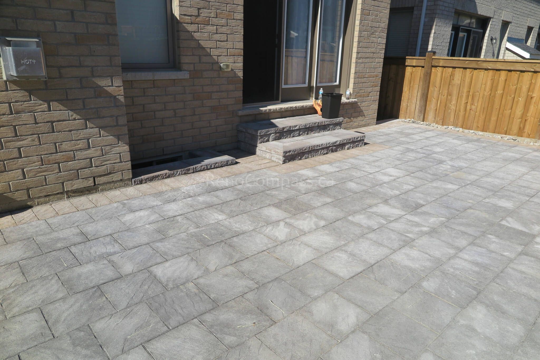 Modern backyard interlocking patio installation in Aurora featuring grey stone pavers, custom front steps, and clean edge detailing along the brick exterior. This professional landscaping and paving project creates a durable, elegant outdoor living and entrance area with a low-maintenance design. Completed by Reno Compass Inc., a trusted Toronto renovation and landscaping contractor serving Aurora and the GTA.