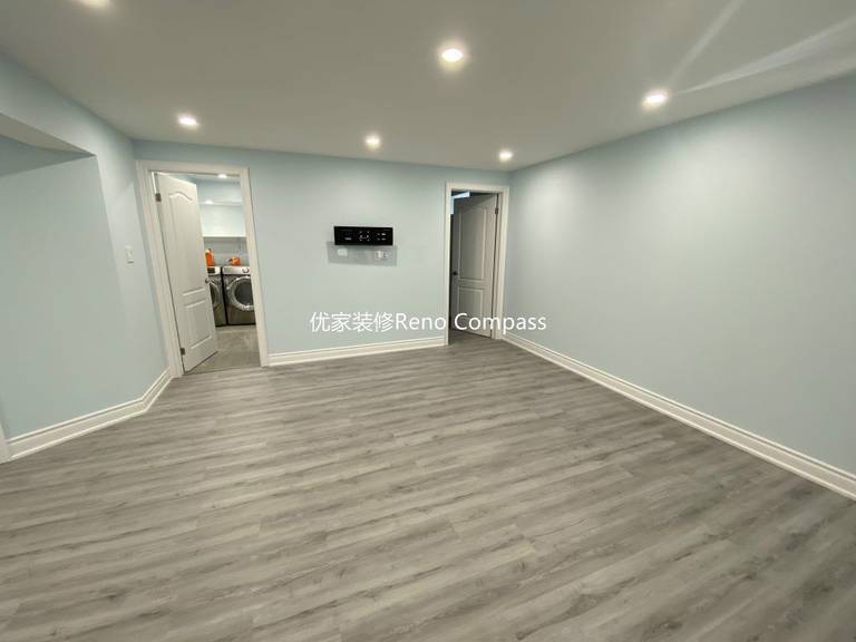 This Aurora basement renovation showcases a spacious open-concept living area completed by a professional Toronto renovation company. The upgraded basement features modern vinyl plank flooring, smooth finished ceilings with LED pot lights, and clean neutral wall tones that enhance brightness and comfort. The open layout seamlessly connects the living space to the laundry and bedroom areas, creating a functional and versatile basement ideal for family entertainment, rental use, or extended living. Contractor: Reno Compass Inc.