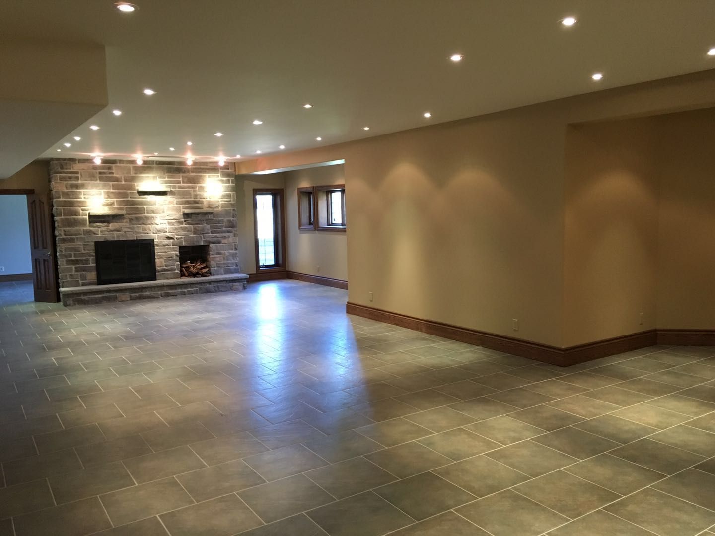 This Toronto interior renovation showcases a spacious open-concept living area designed with modern large-format tile flooring, warm neutral wall tones, and elegant recessed lighting throughout the ceiling. A beautifully crafted stone fireplace feature wall creates a strong focal point, adding both warmth and architectural character to the space. The upgraded lighting layout enhances brightness and visual depth, making the area ideal for entertaining and everyday living. Completed by a professional Toronto renovation company, this project highlights quality finishes, clean design lines, and a refined contemporary interior transformation.
