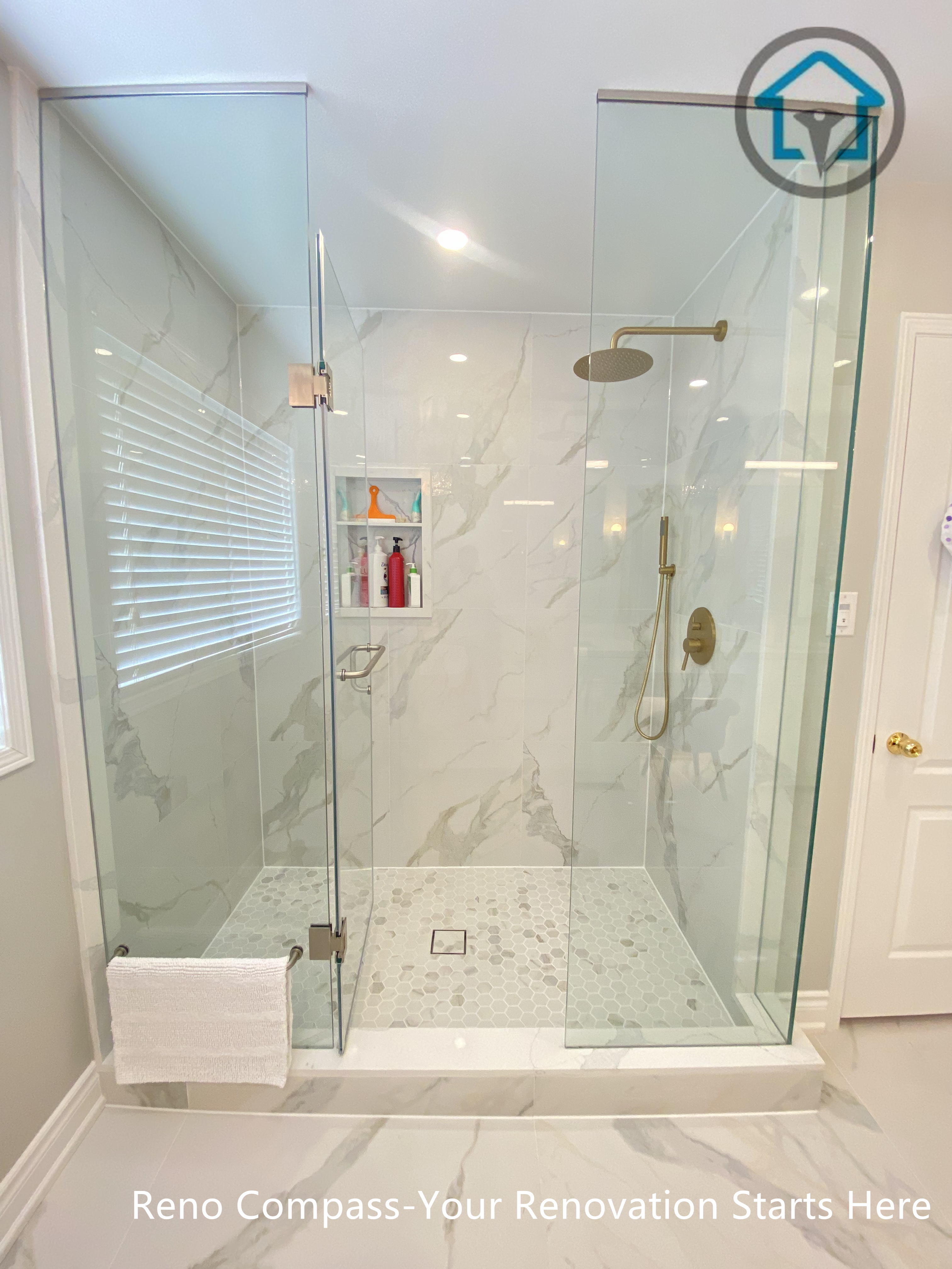 This Mississauga bathroom renovation features a spacious walk-in shower enclosed with frameless clear glass panels to enhance openness and natural light. Large-format marble-look wall tiles are paired with a mosaic tile shower floor for slip resistance and visual contrast. Gold-tone shower fixtures add warmth and elegance, while a built-in wall niche provides functional storage without disrupting the clean layout. The shower design prioritizes comfort, drainage efficiency, and long-term durability through precise detailing and quality materials.