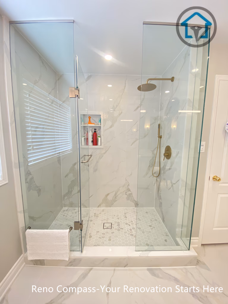 This Mississauga bathroom renovation features a spacious walk-in shower enclosed with frameless clear glass panels to enhance openness and natural light. Large-format marble-look wall tiles are paired with a mosaic tile shower floor for slip resistance and visual contrast. Gold-tone shower fixtures add warmth and elegance, while a built-in wall niche provides functional storage without disrupting the clean layout. The shower design prioritizes comfort, drainage efficiency, and long-term durability through precise detailing and quality materials.