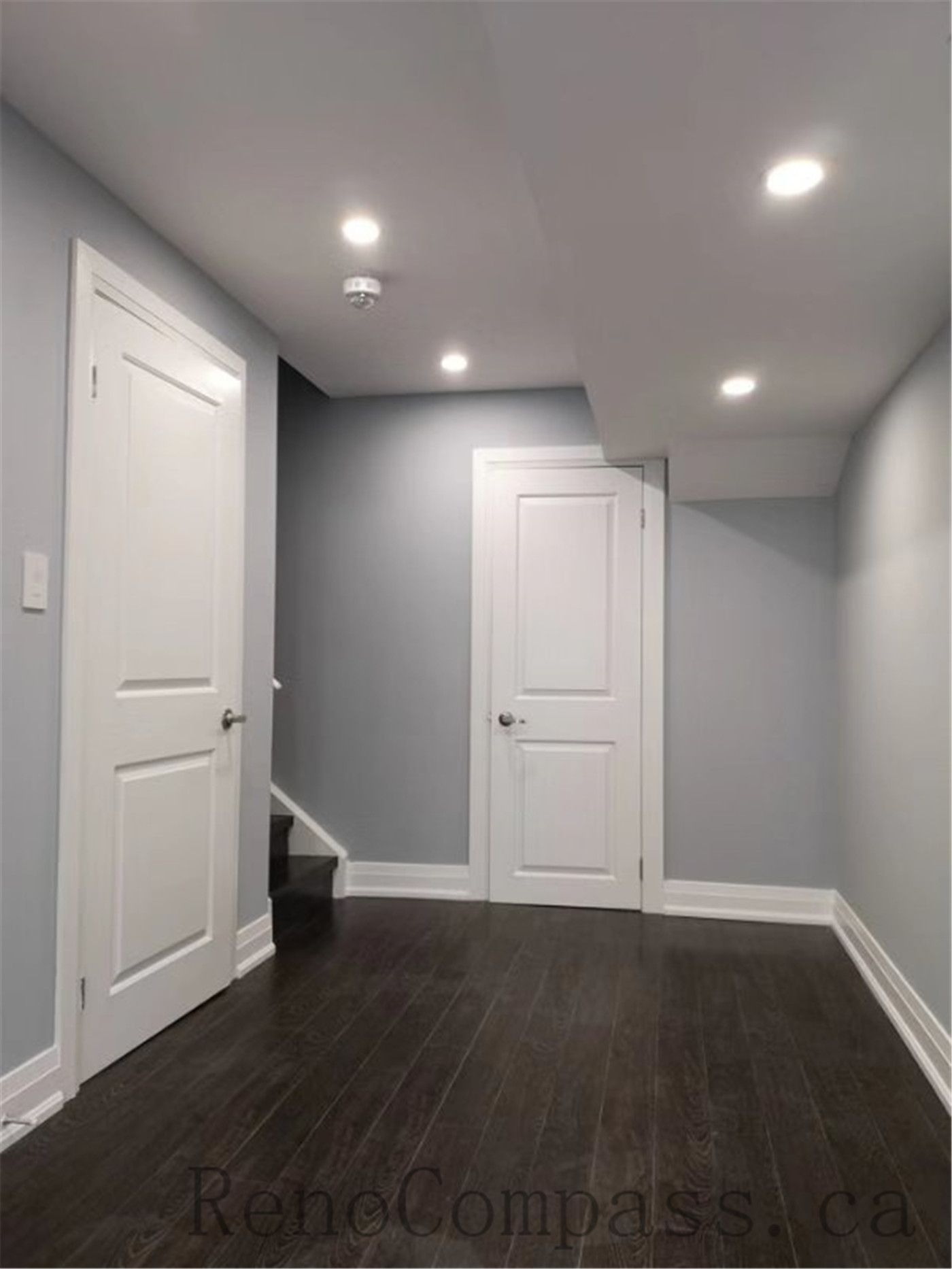 This bright basement hallway in Aurora features recessed ceiling lights, smooth grey walls, and rich dark flooring. A modern minimalist design that enhances the basement’s ambiance and flow, completed by Reno　Compass.