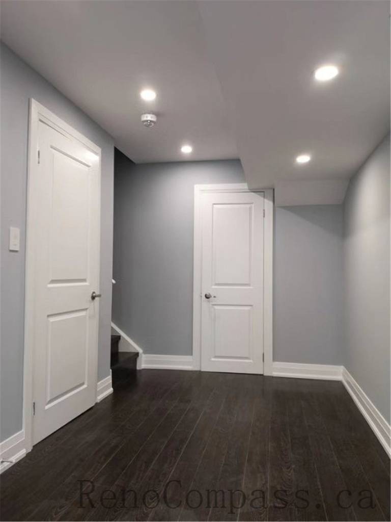 This bright basement hallway in Aurora features recessed ceiling lights, smooth grey walls, and rich dark flooring. A modern minimalist design that enhances the basement’s ambiance and flow, completed by Reno　Compass.
