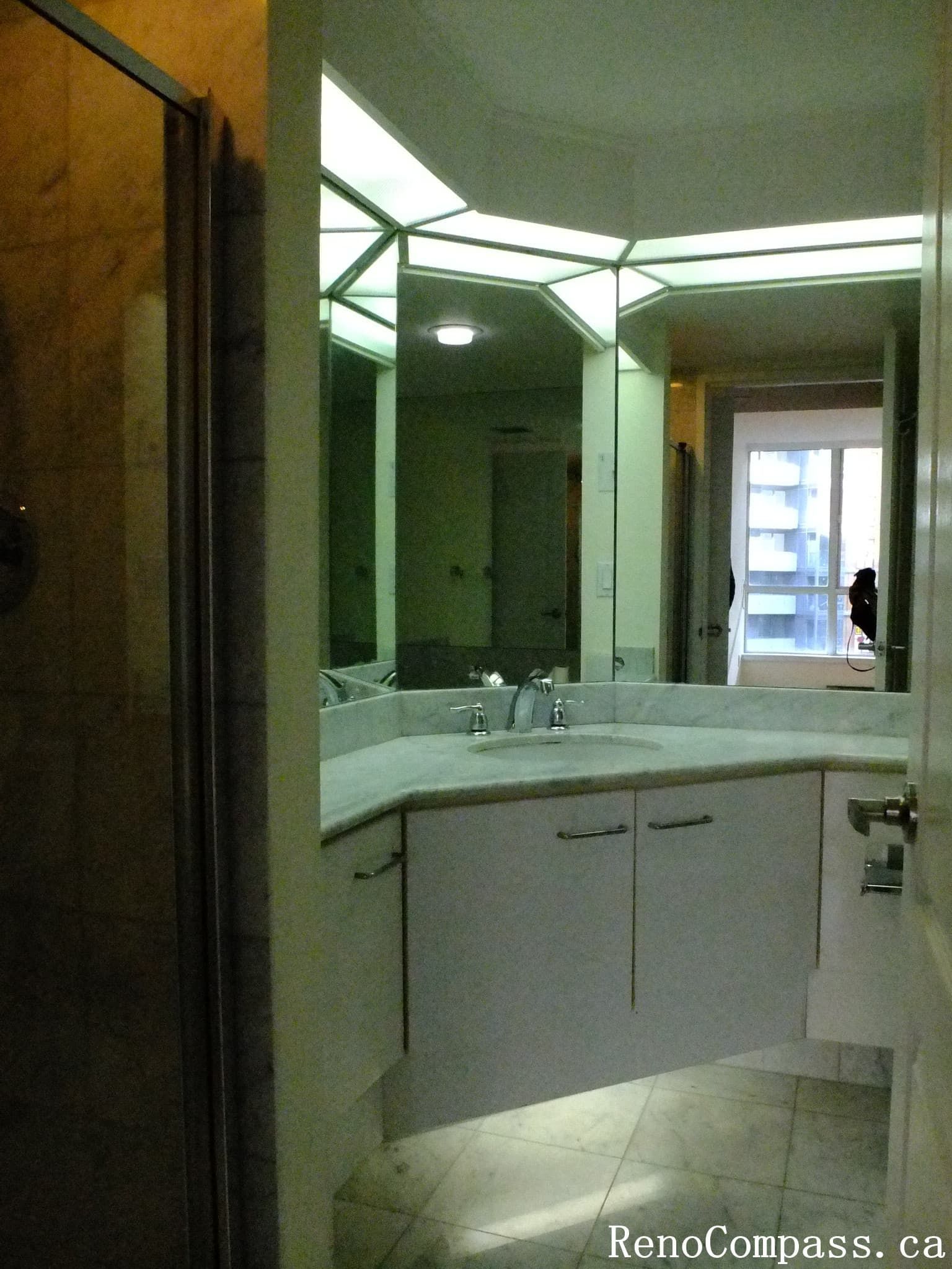 This image shows the original bathroom of a Toronto condominium before renovation. The space features a corner vanity with a marble countertop, mirrored walls, integrated lighting, and a glass shower enclosure. As part of a Toronto interior renovation project, the bathroom was scheduled for upgrades to improve modern design, lighting, and overall functionality.