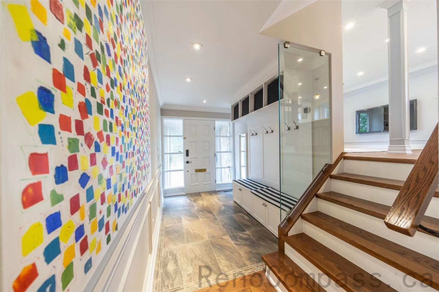 This North York interior renovation features a spacious and well-designed entryway with a custom mudroom bench, coat hooks, and built-in storage. The space includes durable tile flooring, a modern staircase with wood railings, and bright recessed lighting that enhances the welcoming atmosphere. A colorful feature wall adds character and personality to the hallway. Completed by a professional Toronto renovation company, this project blends practical storage solutions with contemporary design to create an organized and stylish home entrance.
