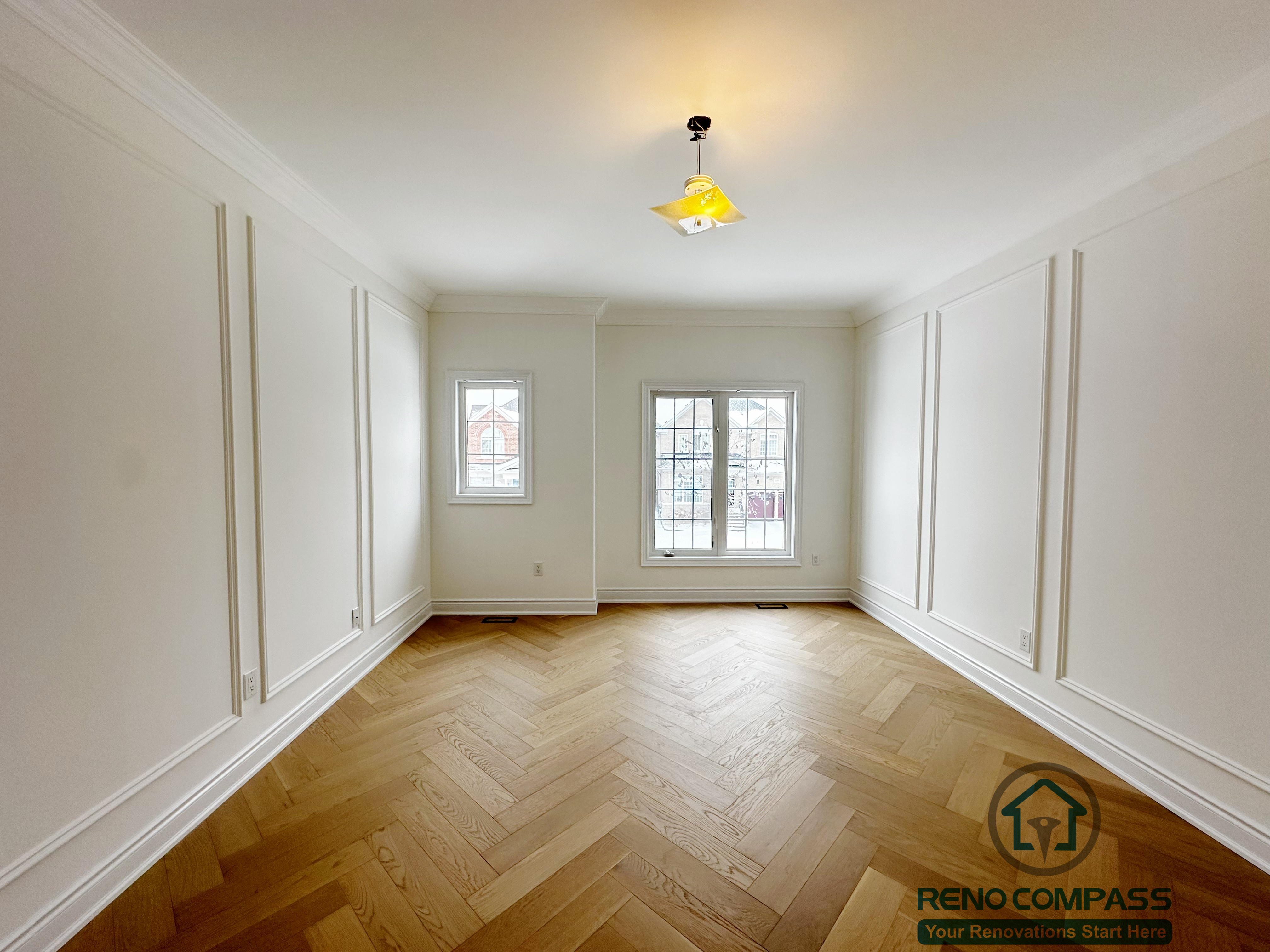Elegant room completed as part of a Vaughan interior renovation, featuring custom wall moulding, crown trim, large windows for natural light, and herringbone-pattern hardwood flooring. The clean white palette and refined detailing create a timeless interior, showcasing the craftsmanship of a professional Toronto renovation company.