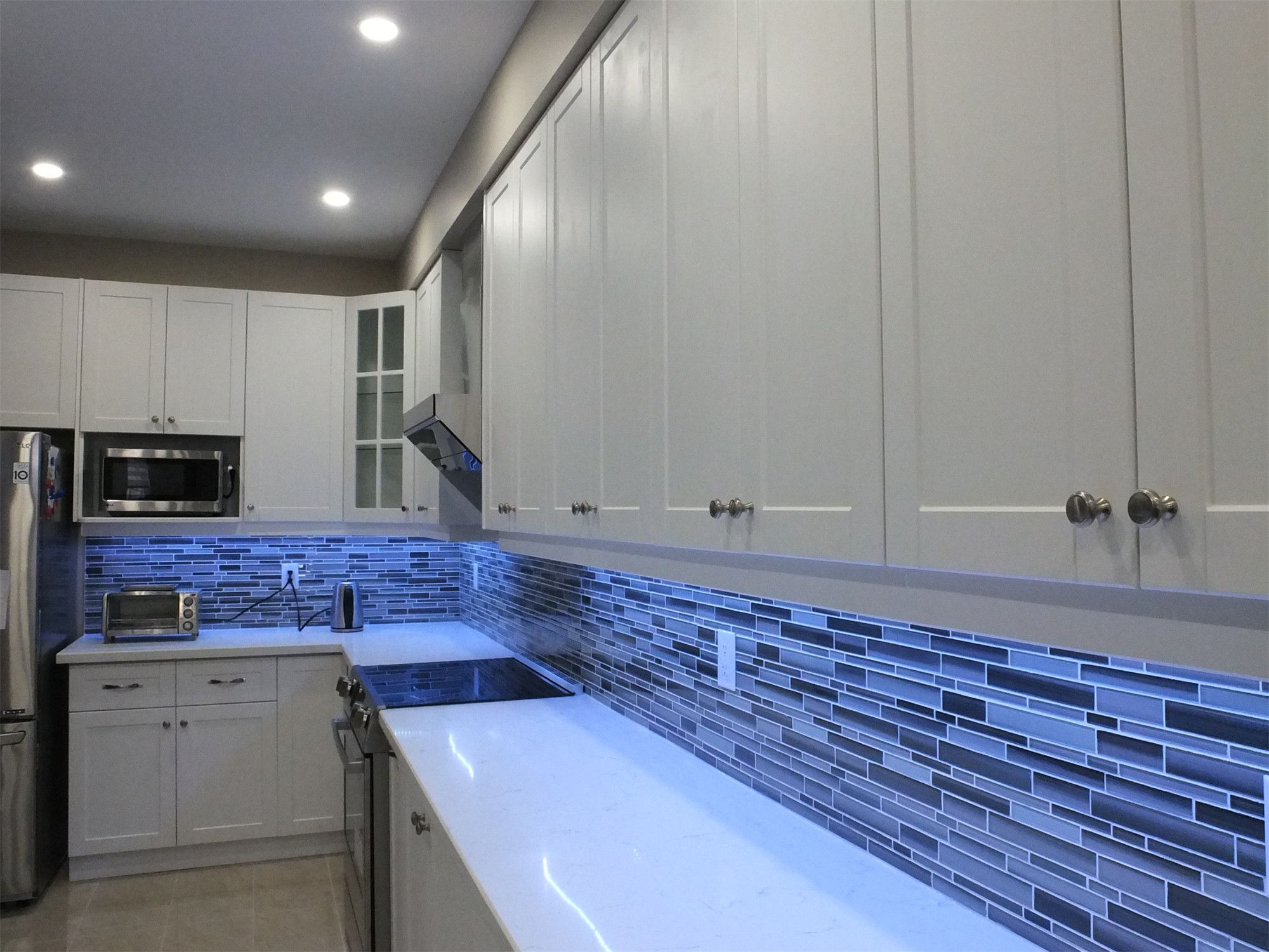 This Vaughan kitchen renovation showcases elegant white shaker cabinetry, quartz countertops, and a modern glass mosaic tile backsplash enhanced with soft LED under-cabinet lighting. The streamlined layout and bright finishes create a clean, contemporary cooking space. Completed by a professional Toronto renovation company, the design blends practical functionality with modern kitchen aesthetics.