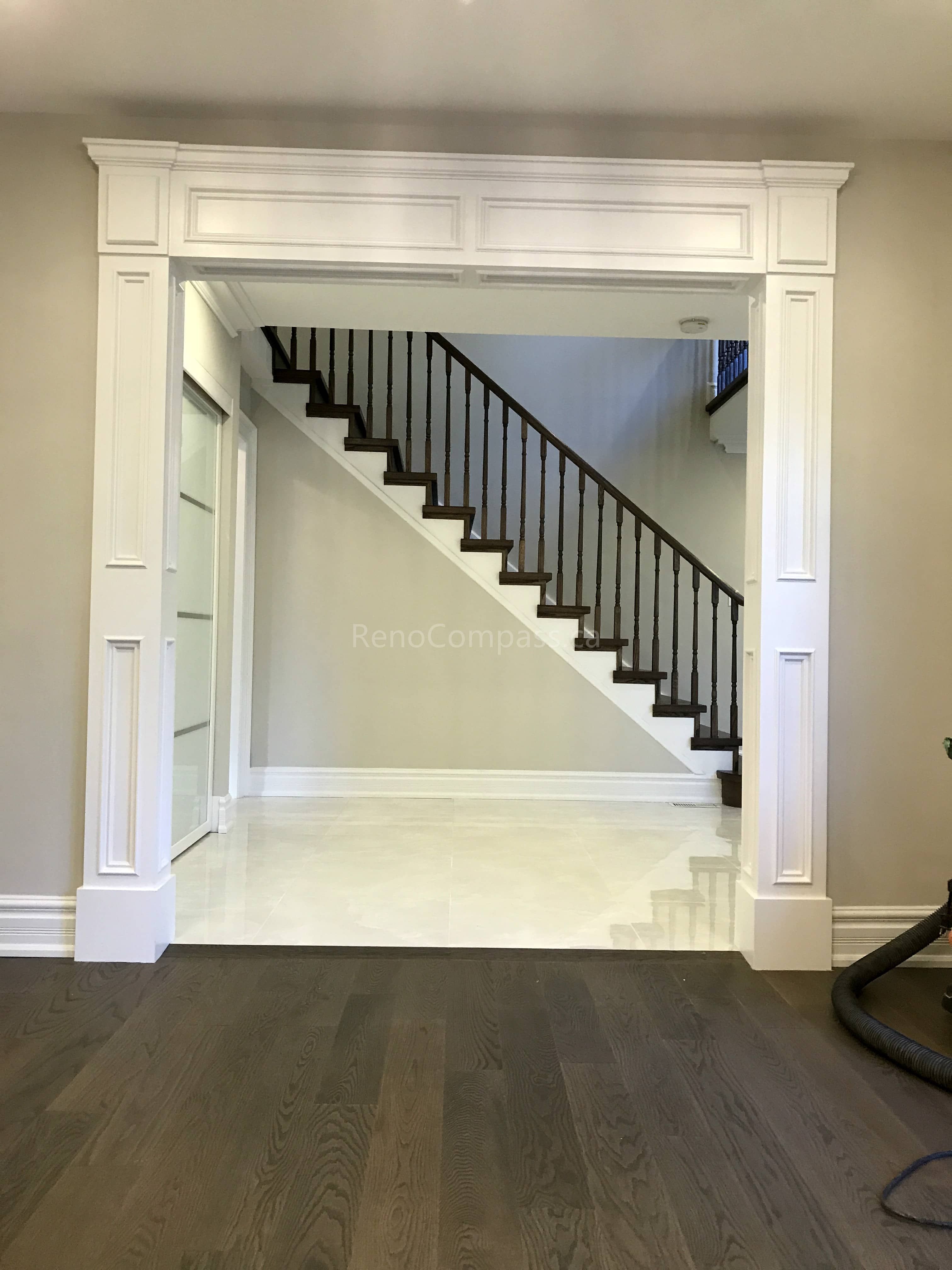 This Toronto interior renovation by Reno Compass showcases custom millwork detailing with a decorative archway entrance and upgraded staircase design. Elegant trim work and panel molding add architectural depth and a refined, classic look to the space. The combination of new flooring, fresh paint, and enhanced layout creates a bright and welcoming interior that blends modern comfort with timeless craftsmanship, increasing both style and property value.