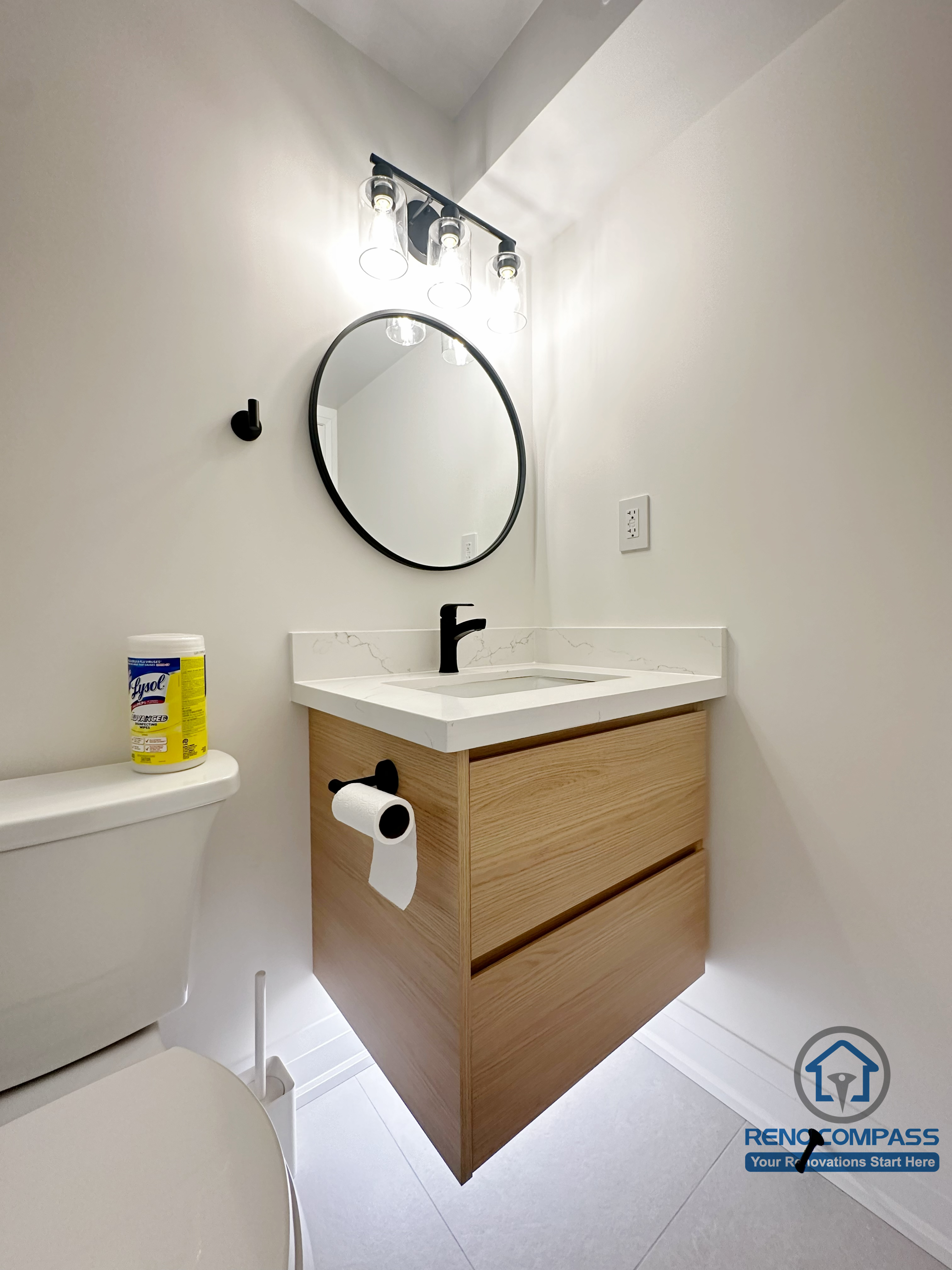 Modern basement bathroom renovation in Markham featuring a glass-enclosed shower, wall-mounted vanity with wood finish, round mirror, and clean contemporary fixtures. Designed for efficient use of space, durability, and everyday comfort.