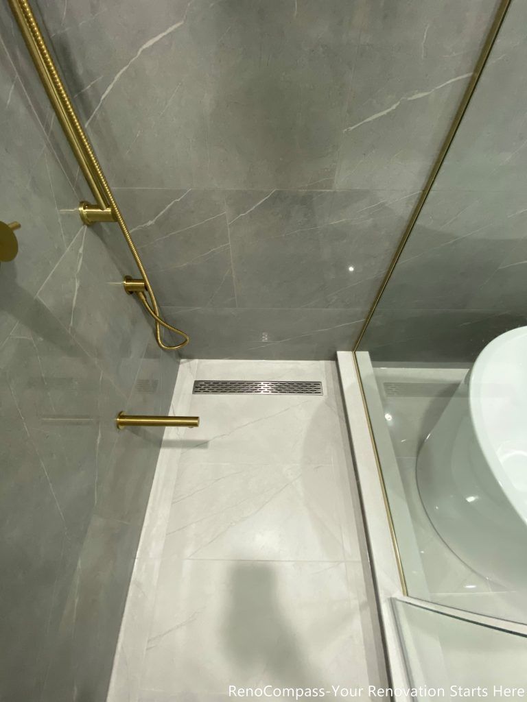 This Oakville master bathroom renovation highlights a modern walk-in shower with sleek linear floor drain, large-format porcelain tiles, and premium gold shower fixtures. The clean tile layout, precise slope for drainage, and frameless glass enclosure create a seamless and contemporary spa-style shower experience. Completed by a trusted Toronto renovation company, this bathroom upgrade focuses on waterproofing quality, functionality, and elegant design, delivering a durable and visually refined space that enhances everyday comfort and home value.