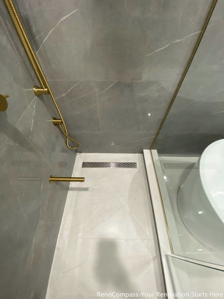 This Oakville master bathroom renovation highlights a modern walk-in shower with sleek linear floor drain, large-format porcelain tiles, and premium gold shower fixtures. The clean tile layout, precise slope for drainage, and frameless glass enclosure create a seamless and contemporary spa-style shower experience. Completed by a trusted Toronto renovation company, this bathroom upgrade focuses on waterproofing quality, functionality, and elegant design, delivering a durable and visually refined space that enhances everyday comfort and home value.