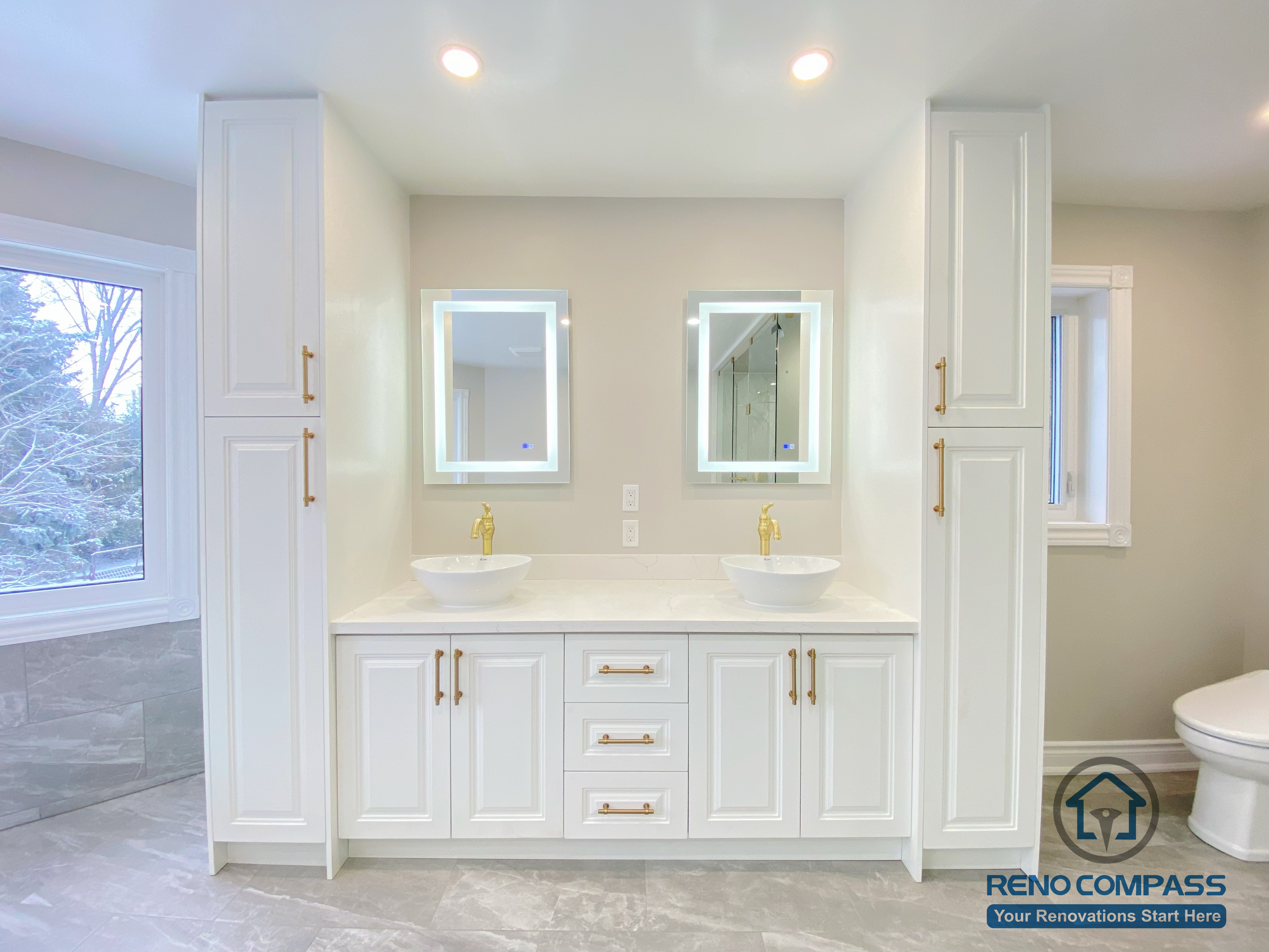 This Richmond Hill bathroom renovation features a custom-built double vanity with integrated storage cabinets and symmetrical design. The white cabinetry is paired with gold hardware, vessel sinks, and backlit mirrors, creating a clean and elegant focal point. Tall storage towers on both sides enhance functionality while maintaining visual balance. This vanity area reflects thoughtful space planning, refined material selection, and high-quality craftsmanship in a modern bathroom renovation project in Richmond Hill.