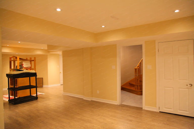 This image features an open-concept basement renovation in Markham, highlighting the spacious layout, structural support column, and evenly distributed recessed lighting. The finished basement includes durable flooring, smooth wall finishes, and clearly defined functional zones while maintaining an open and flexible living area. This design maximizes usable space and long-term comfort, reflecting the craftsmanship of a professional Toronto renovation company specializing in basement remodeling.