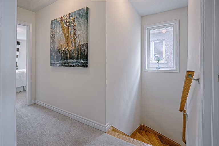 This upper floor landing renovation showcases a bright transitional space connecting bedrooms with a clean, neutral design. Soft carpeting enhances comfort, while natural light from the side window improves brightness and openness. The finished wooden stair edge detail adds warmth and craftsmanship to the transition between levels. Completed by a professional Toronto renovation company, this interior upgrade emphasizes smooth circulation, refined finishes, and cohesive modern residential design.