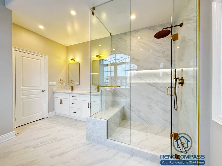 Full view of a Vaughan primary bathroom renovation showcasing a custom double vanity with quartz countertop, gold fixtures, LED mirror lighting, and a frameless glass walk-in shower finished with marble-look porcelain tile. The layout maximizes light, storage, and circulation, completed by a professional Toronto renovation company specializing in high-end bathroom design.