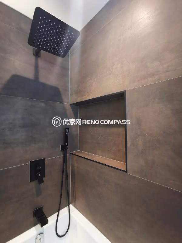 Walk-in shower detail from a North York interior renovation, featuring a ceiling-mounted rainfall showerhead, matte black fixtures, and a recessed wall niche for built-in storage. Large-format wall tiles create a seamless, low-maintenance surface while maintaining a modern, spa-inspired aesthetic. The clean layout and integrated detailing reflect a bathroom renovation completed by a Toronto renovation company focused on durability, functionality, and refined construction quality.