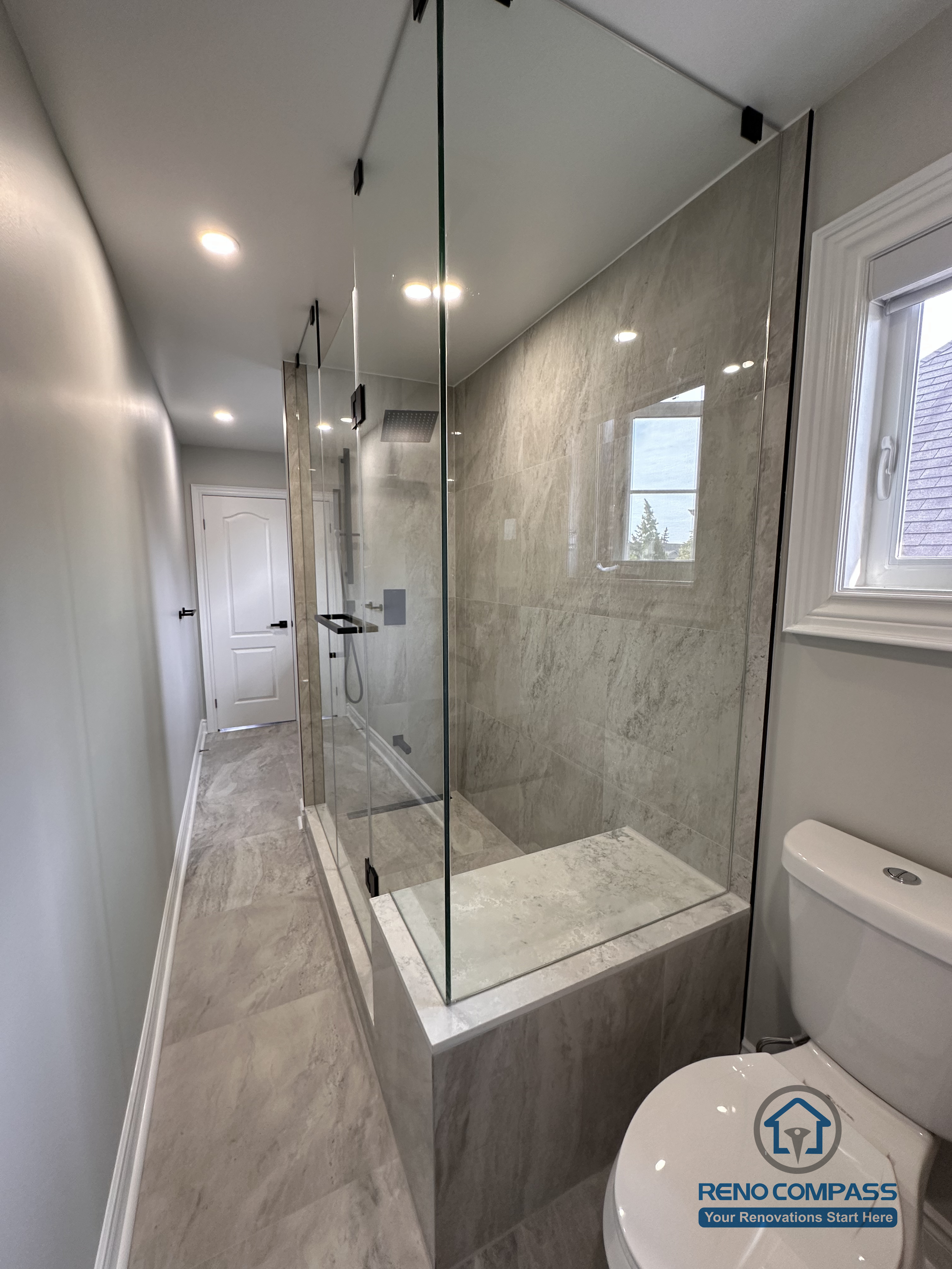 This Markham bathroom renovation highlights a glass-enclosed tub and shower combination with full-height stone-look wall tiles and matte black hardware. The design maintains openness while ensuring practical water control and durability. Completed by a professional Toronto renovation company, Reno Compass Inc., the bathroom reflects clean detailing, balanced proportions, and long-term functionality.