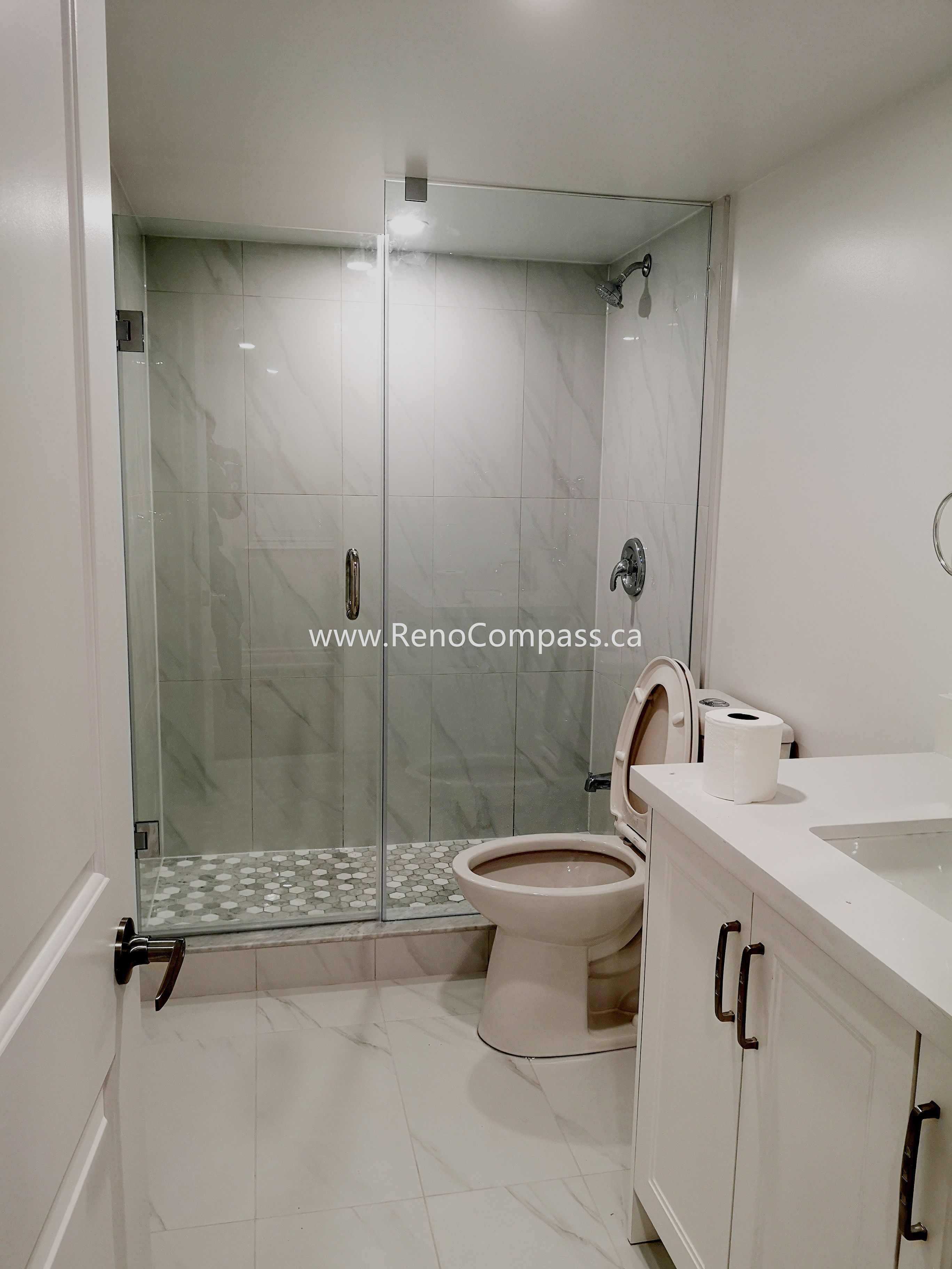 This Vaughan basement bathroom renovation showcases a modern glass shower enclosure with elegant marble-style wall tiles and a clean, minimalist layout. The upgraded space includes a sleek vanity, contemporary fixtures, and durable floor tiles designed for both style and functionality. Completed by Reno Compass Inc., this basement bathroom upgrade enhances comfort, increases home value, and creates a bright, modern space that complements the fully renovated basement.