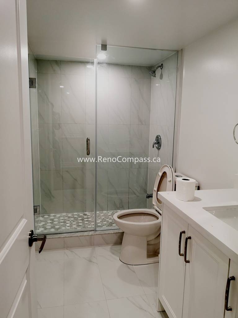 This Vaughan basement bathroom renovation showcases a modern glass shower enclosure with elegant marble-style wall tiles and a clean, minimalist layout. The upgraded space includes a sleek vanity, contemporary fixtures, and durable floor tiles designed for both style and functionality. Completed by Reno Compass Inc., this basement bathroom upgrade enhances comfort, increases home value, and creates a bright, modern space that complements the fully renovated basement.