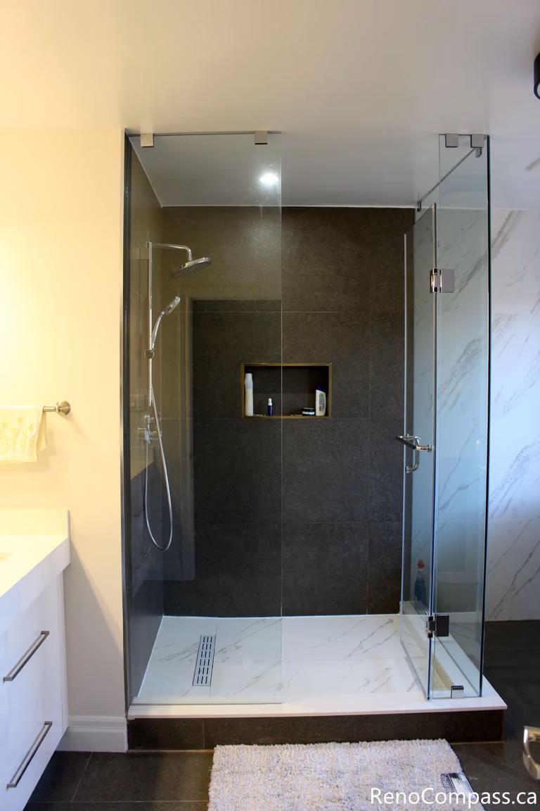 This Mississauga bathroom renovation features a walk-in glass shower with a built-in wall niche, large-format wall tiles, and a linear floor drain. The frameless enclosure and clean tile layout create a modern, functional shower space designed for comfort, durability, and easy maintenance.
