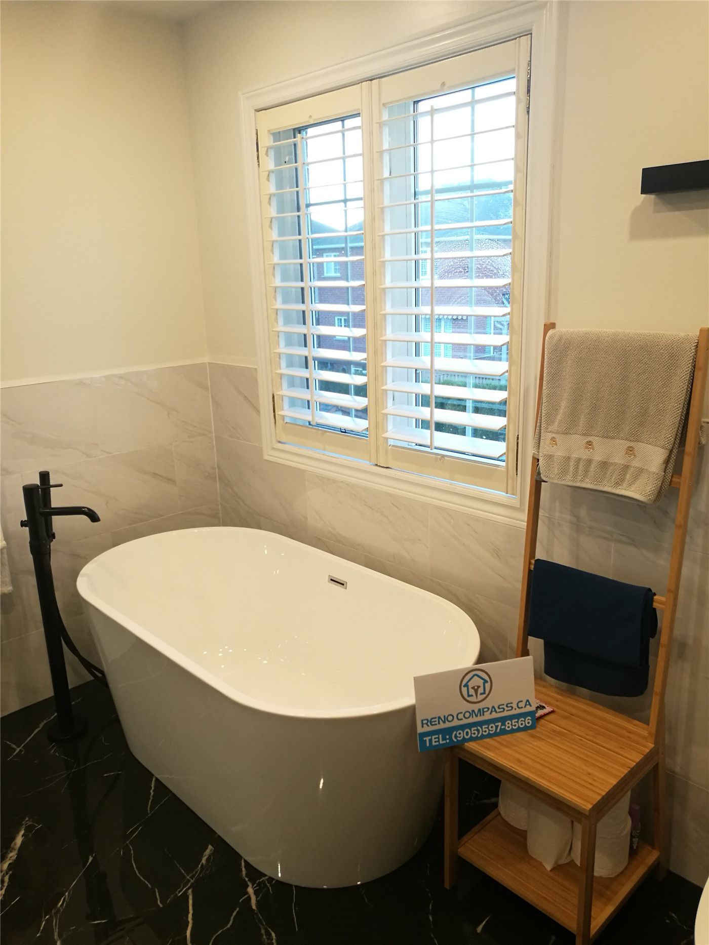 This Richmond Hill bathroom renovation showcases a sleek freestanding bathtub paired with a modern black floor-mounted faucet and marble-style wall finishes. Natural light from the large window enhances the clean, spa-inspired atmosphere, while thoughtful details like towel storage and durable flooring improve everyday functionality. Completed by a trusted Toronto renovation company, this project highlights elegant design, quality materials, and practical luxury for contemporary homes.