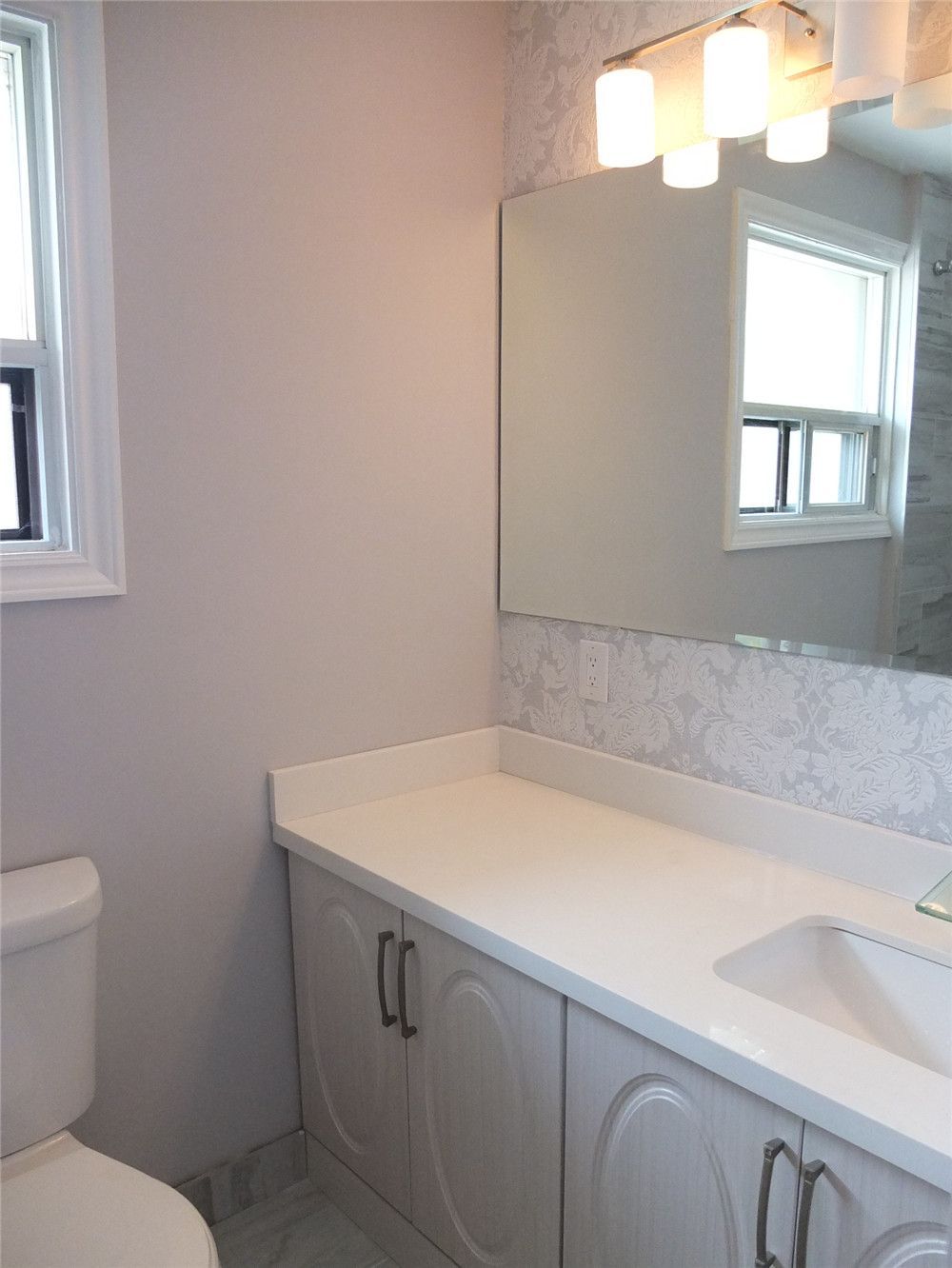 This North York bathroom renovation features a clean and functional vanity area with a quartz countertop, integrated sink, large mirror, and modern wall lighting. The bright finishes and efficient layout help maximize space while improving everyday usability. Completed by a professional Toronto renovation team, the design focuses on simplicity, durability, and a fresh contemporary bathroom style.