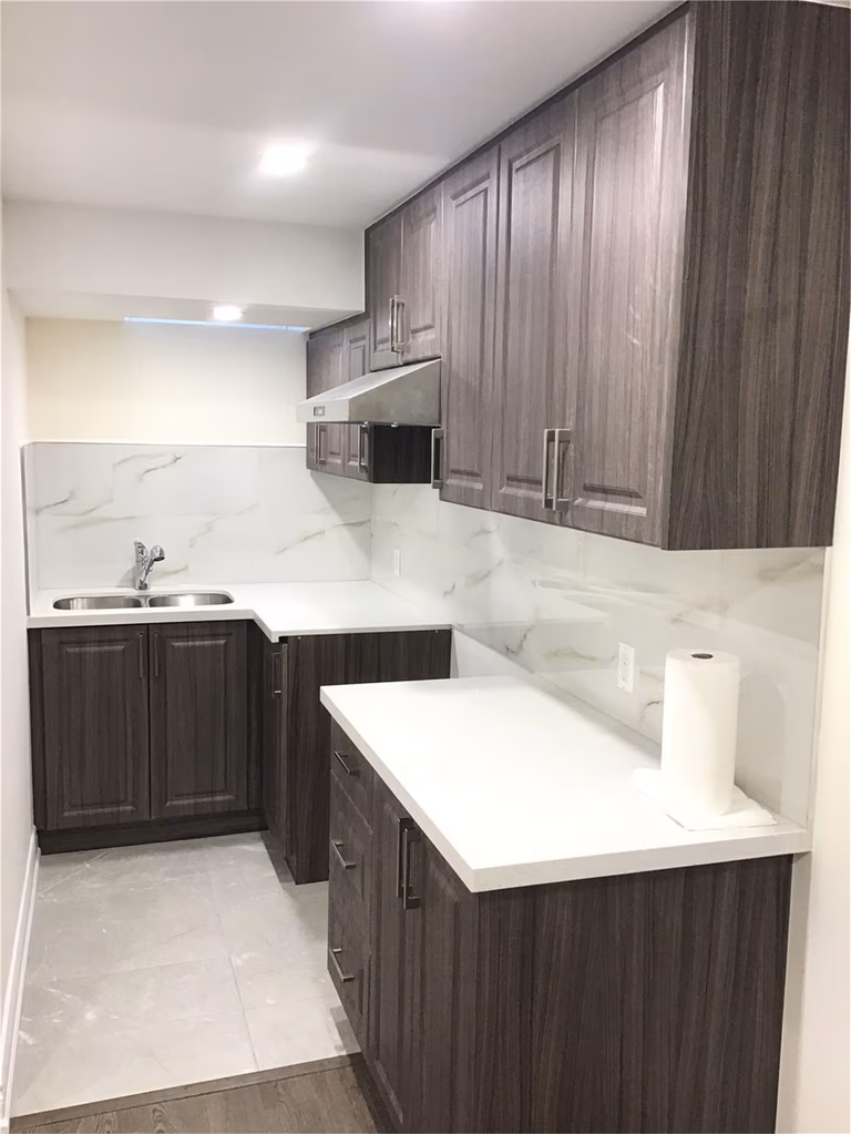 This Mississauga basement renovation includes a compact and modern kitchenette featuring dark wood cabinets, a sleek quartz countertop, and marble-style backsplash. The efficient layout maximizes functionality, making it perfect for a secondary suite, rental unit, or in-law living space.