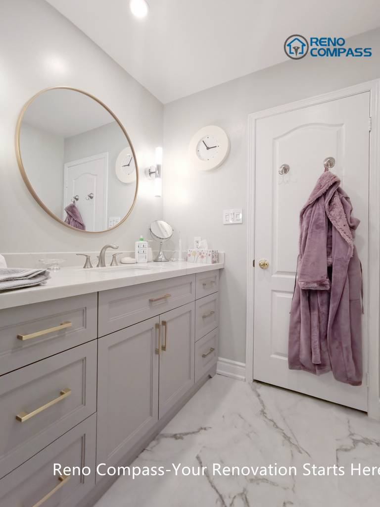 This Mississauga bathroom renovation features a custom vanity with soft grey cabinetry, brushed gold hardware, and a clean quartz countertop. A round framed mirror paired with vertical wall sconces provides balanced lighting for daily use while enhancing the overall elegance of the space. Thoughtful storage design and refined finishes reflect the attention to detail and craftsmanship expected from a professional Toronto renovation company.