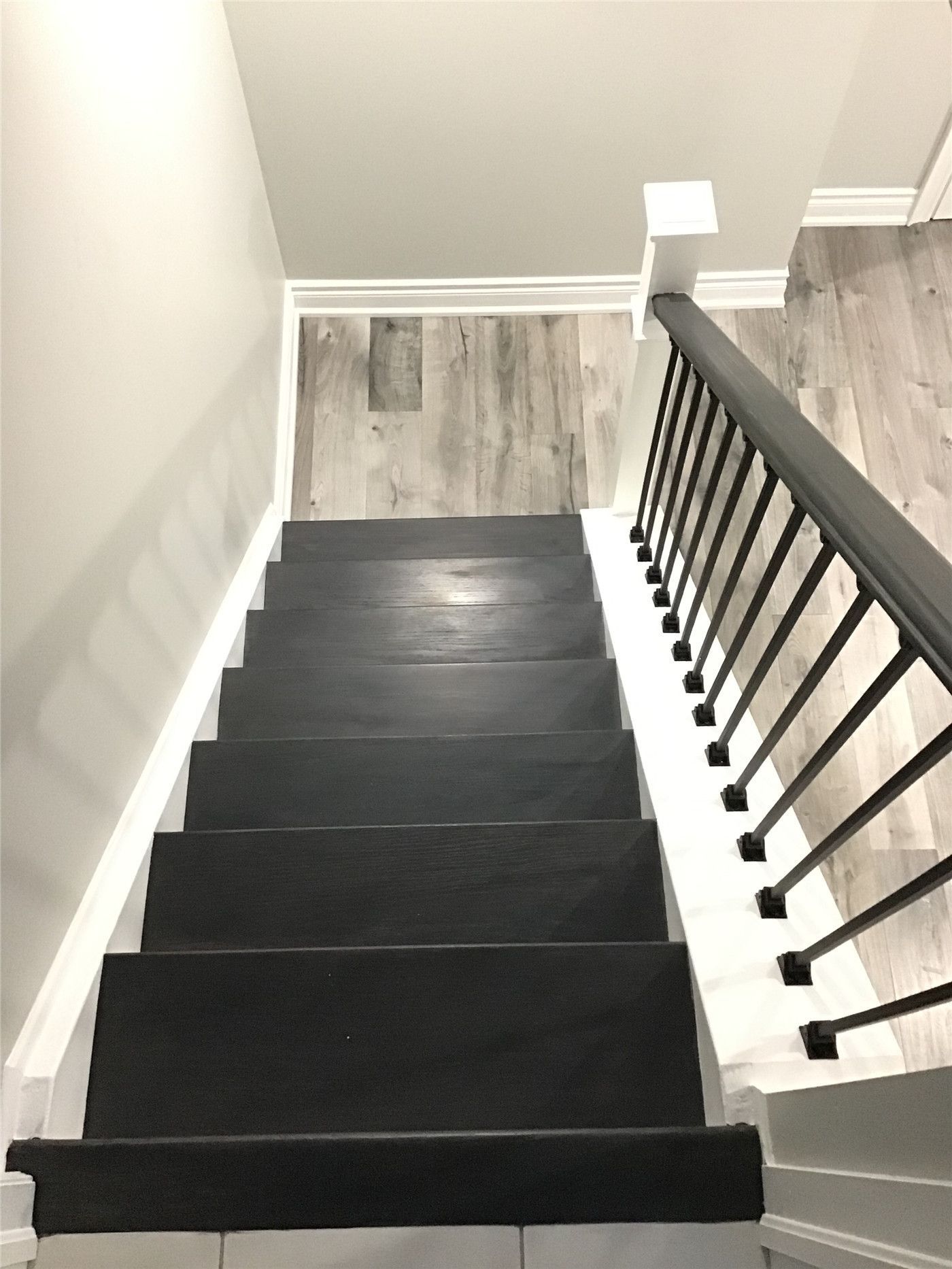 Basement staircase renovation in Newmarket featuring dark stained wood treads, white risers, and sleek black metal railings. This stylish stair upgrade seamlessly connects the main floor to the newly finished basement while enhancing safety and visual appeal.