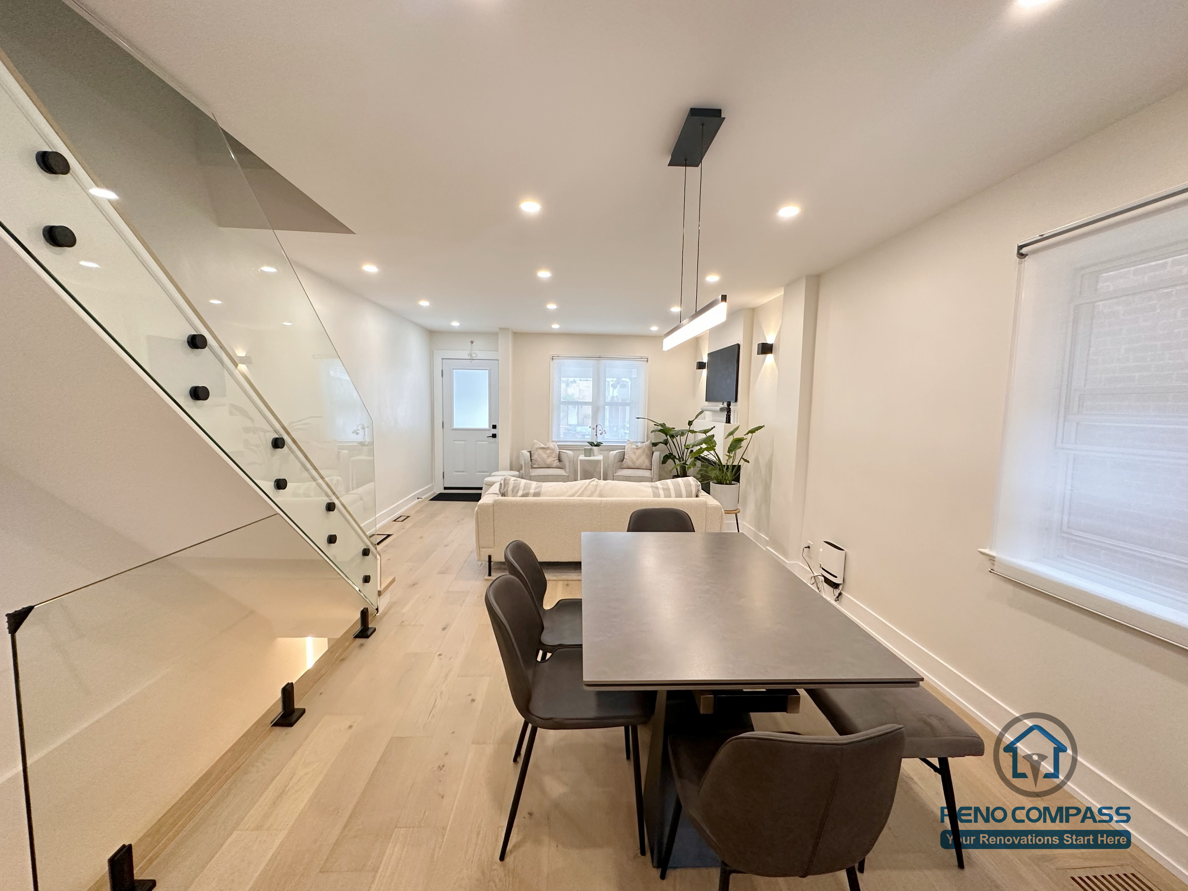 This Toronto interior renovation captures a seamless transition from the dining area to the living space, featuring wide-plank hardwood flooring, recessed ceiling lighting, and a contemporary glass staircase. The open layout enhances spatial flow and brightness, reflecting the refined planning and execution of a professional Toronto renovation company.