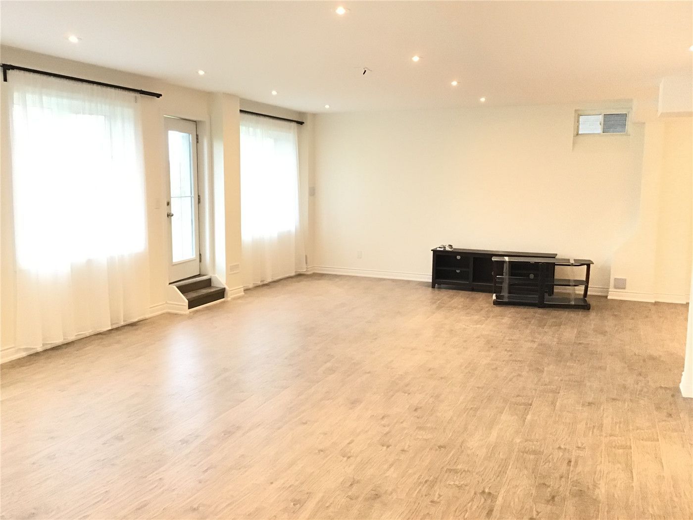 This Aurora interior renovation showcases a bright and spacious open-concept basement living area, featuring durable wood-look vinyl flooring, recessed pot lighting, and large windows that maximize natural light. The clean layout and neutral tones create a modern, functional space ideal for entertainment or family use.