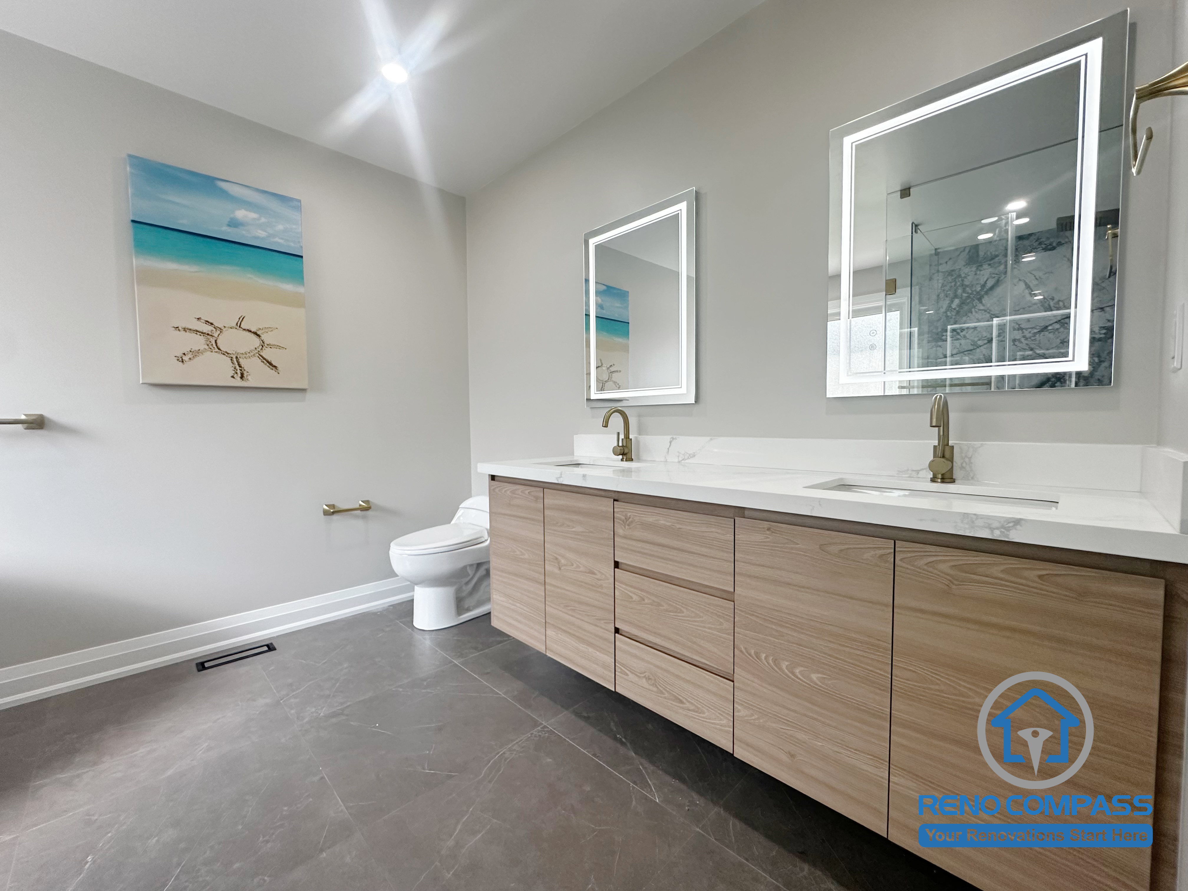 This Oakville bathroom renovation highlights a functional double vanity with warm wood cabinetry, integrated storage, and backlit mirrors that provide even, comfortable lighting. The layout prioritizes daily usability, clear sightlines, and balanced proportions, creating a calm and practical bathroom environment. Designed and completed by Reno Compass for a modern Oakville home.
