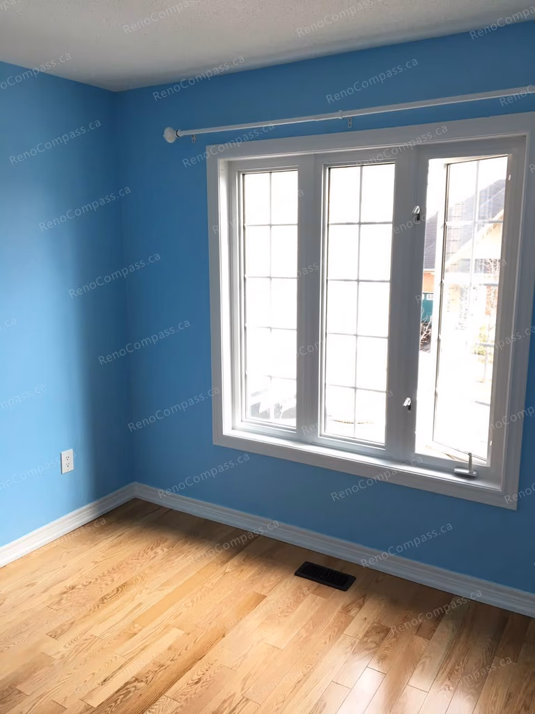 This Markham interior renovation showcases a refreshed bedroom with new hardwood flooring, smooth ceiling finish, and vibrant blue wall painting. Large windows bring in natural light, enhancing the clean and comfortable living space. Completed by Reno Compass, a trusted Toronto renovation company specializing in high-quality interior upgrades and modern home improvements.