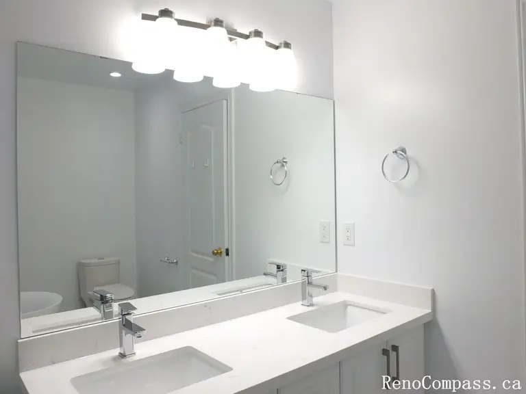 This Richmond Hill bathroom renovation features a modern double-sink vanity with a sleek quartz countertop and full-width mirror enhanced by bright LED vanity lighting. Completed by a professional Toronto renovation company, the space is designed for improved functionality, balanced illumination, and clean contemporary aesthetics. The streamlined fixtures and neutral palette create a bright, organized, and practical bathroom layout ideal for everyday family use.