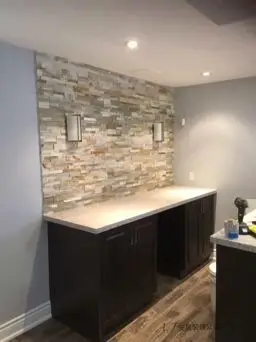 Interior renovation in Scarborough featuring a decorative stone feature wall, custom dark cabinetry, recessed lighting, and modern flooring, creating a stylish and functional living space.