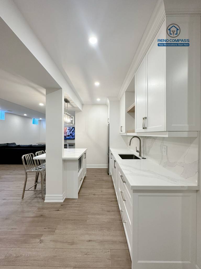 The basement kitchenette features custom white cabinetry, quartz countertops, and a functional island for casual seating. Designed as part of a full Bradford basement renovation, this space balances style and efficiency, making it ideal for extended family use, entertaining, or future rental potential.
