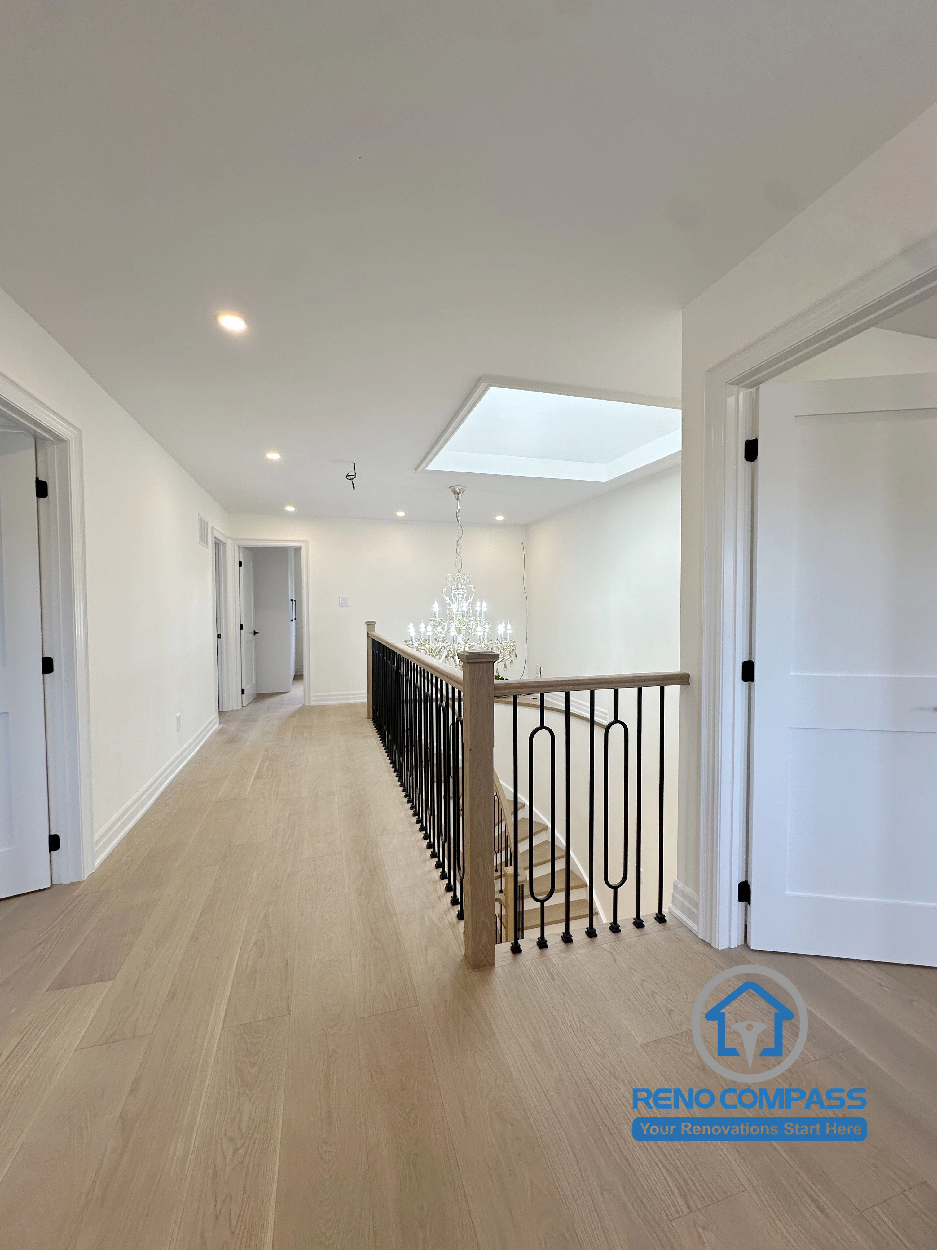 A bright second-floor hallway featuring an open-to-below layout, custom black metal railings, natural oak flooring, and a skylight that fills the space with natural light. Completed as part of a luxury whole home renovation in Markham, Ontario, this modern interior design showcases elegant craftsmanship and seamless architectural flow by Reno Compass.