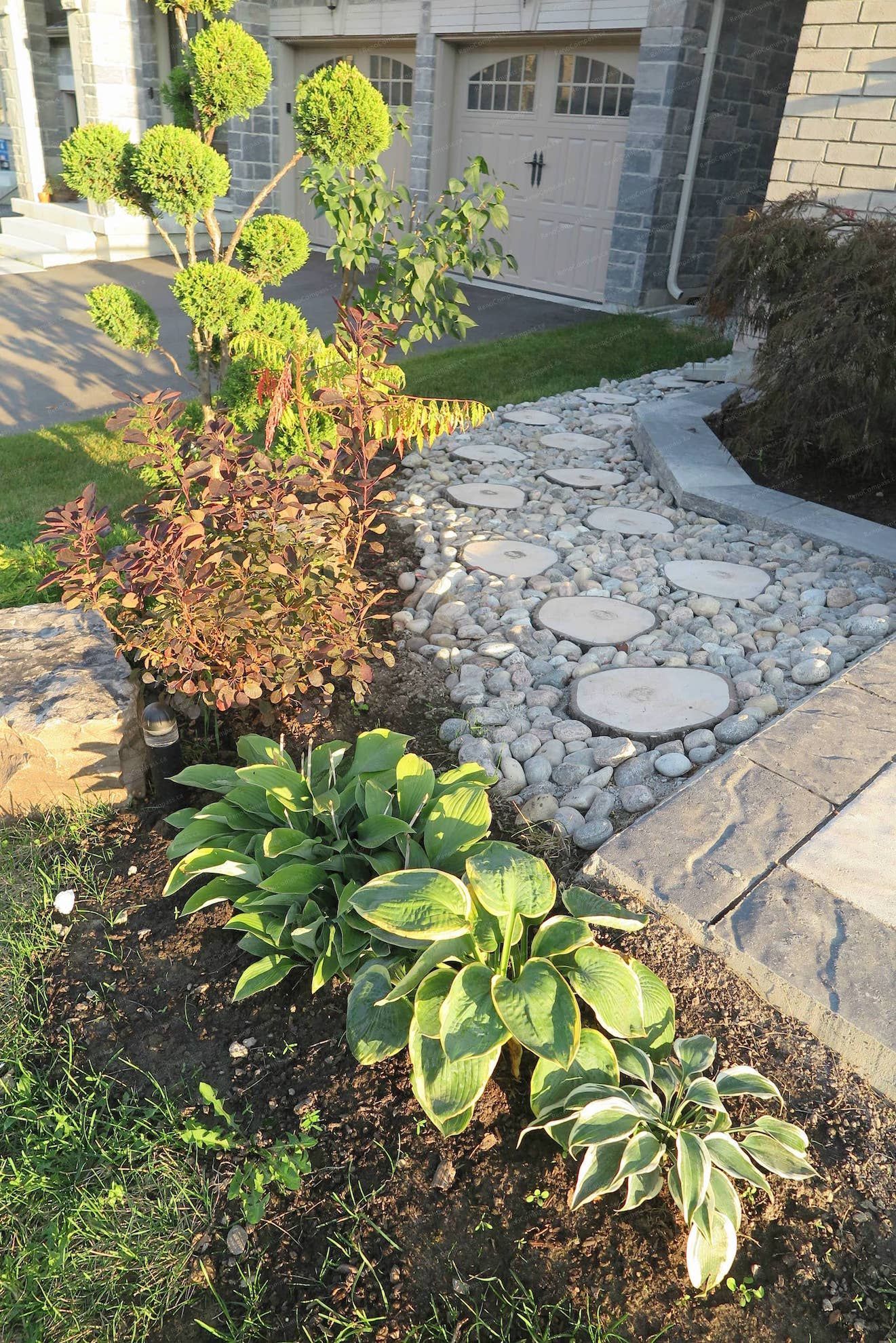 This Vaughan landscaping project features a stamped concrete driveway paired with decorative river rock garden borders and low-maintenance shrubs. The clean layout enhances drainage, visual balance, and curb appeal while complementing the modern garage entrance and exterior stone façade. Professionally completed by Reno Compass Inc. 🌿🏡